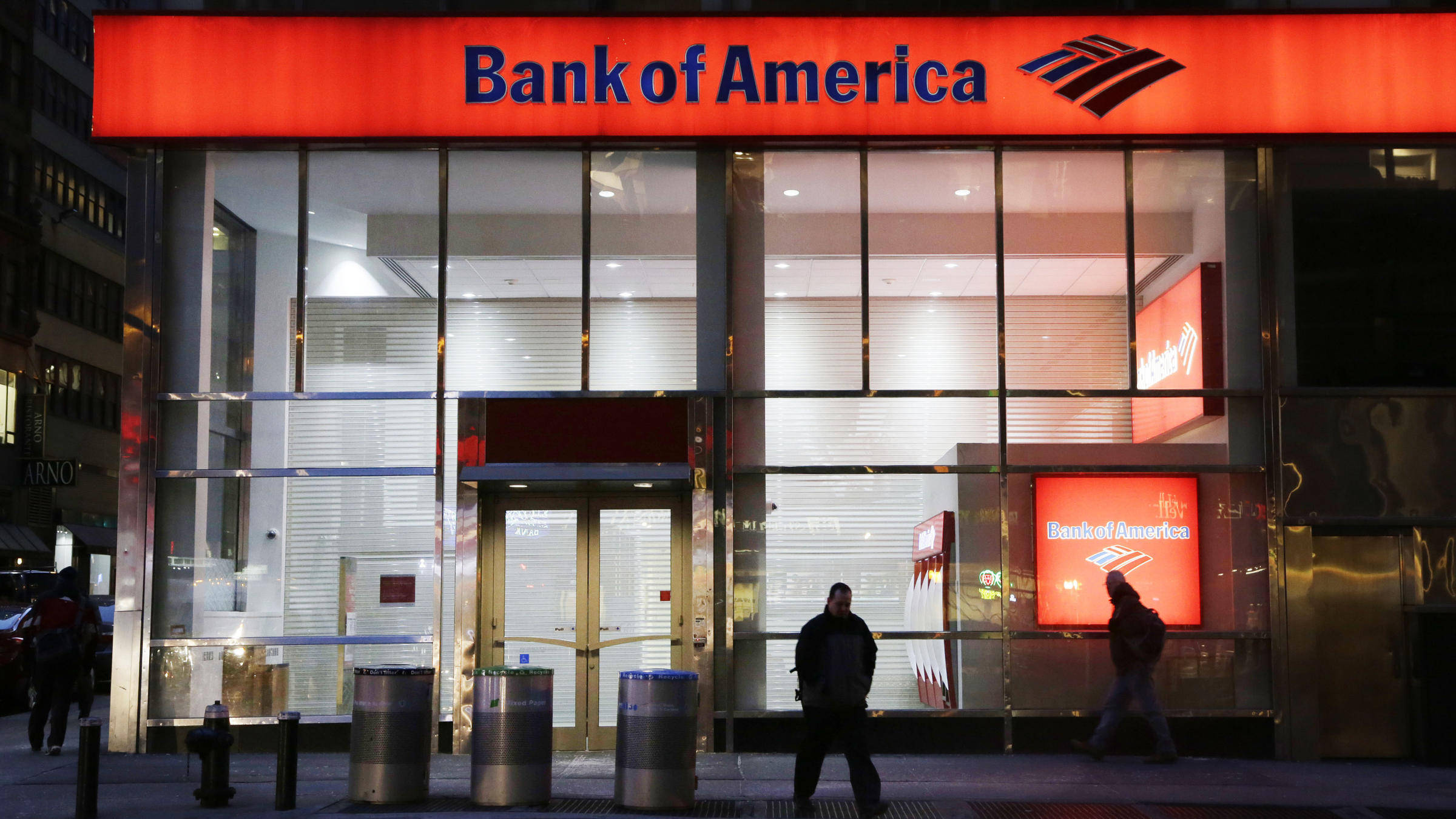美國銀行夜間外觀 壁紙 — 夜晚，行人走過時，一個發光的紅色 Bank of America 標誌照亮了玻璃幕牆的市區銀行。