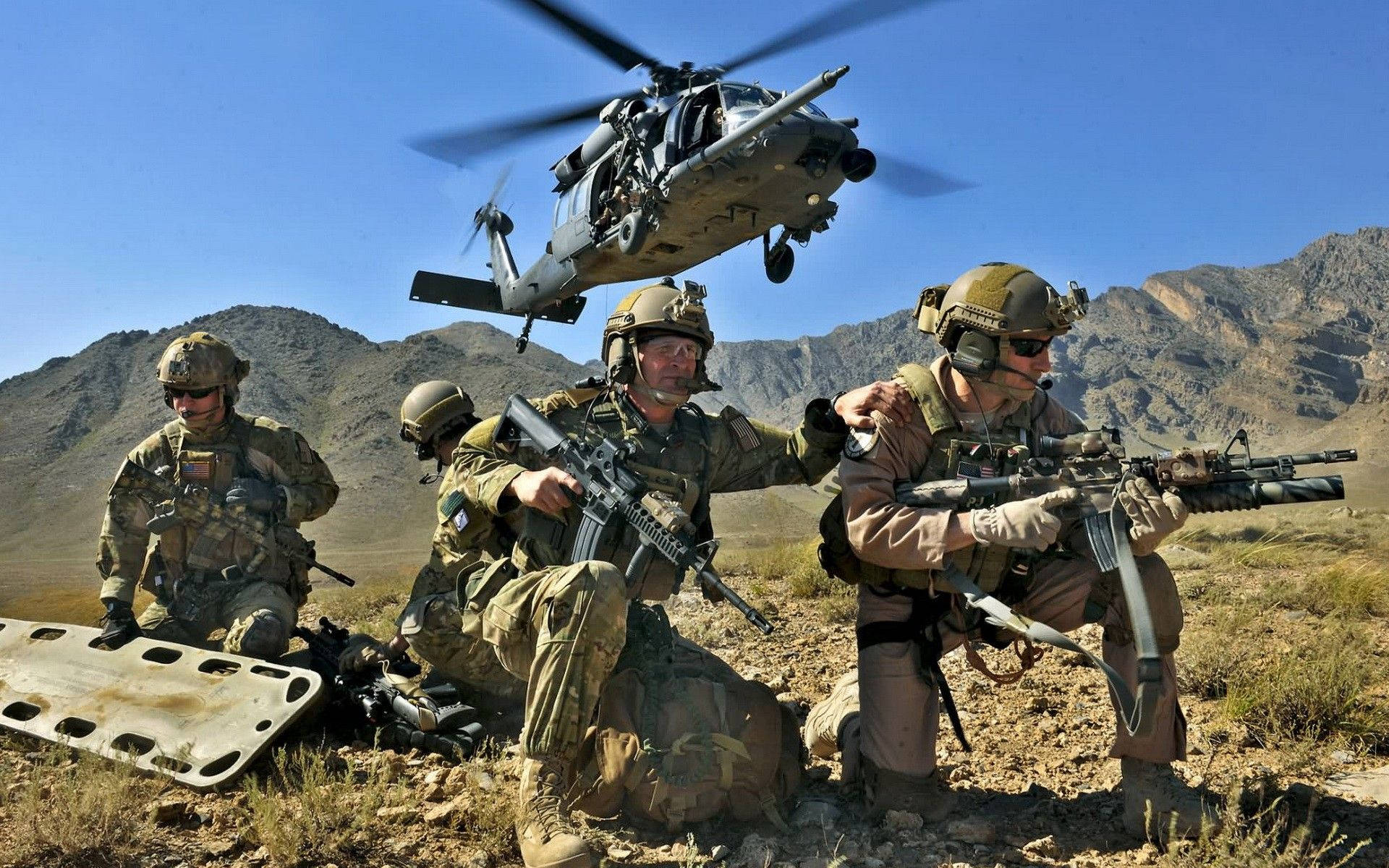 穿著沙漠裝備的士兵蹲下持步槍，一架直升機在岩石山脈上空盤旋。