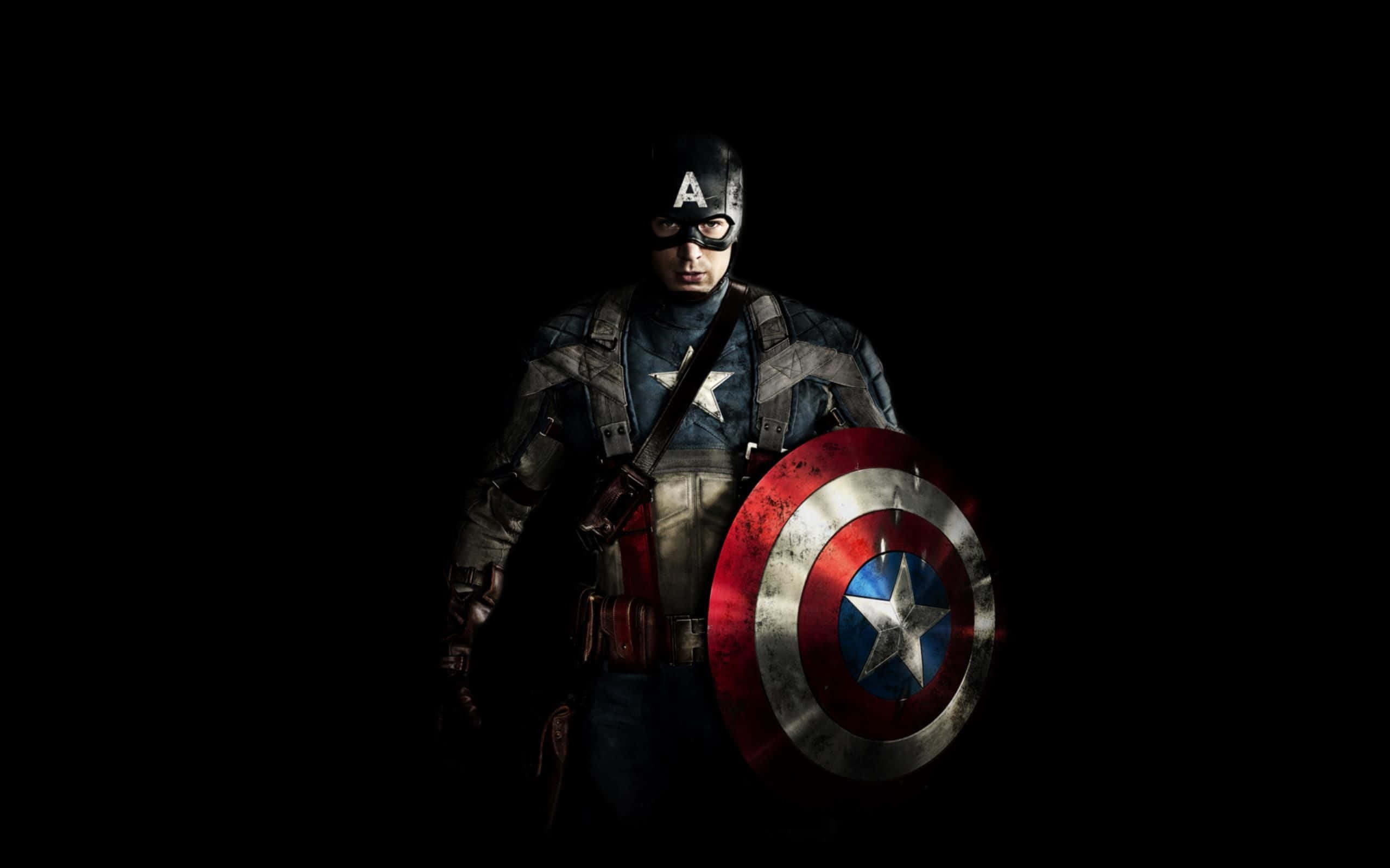 Best Captain America 桌布 壁紙 — 美國隊長站在黑暗中，手持標誌性盾牌，表情嚴肅堅定。