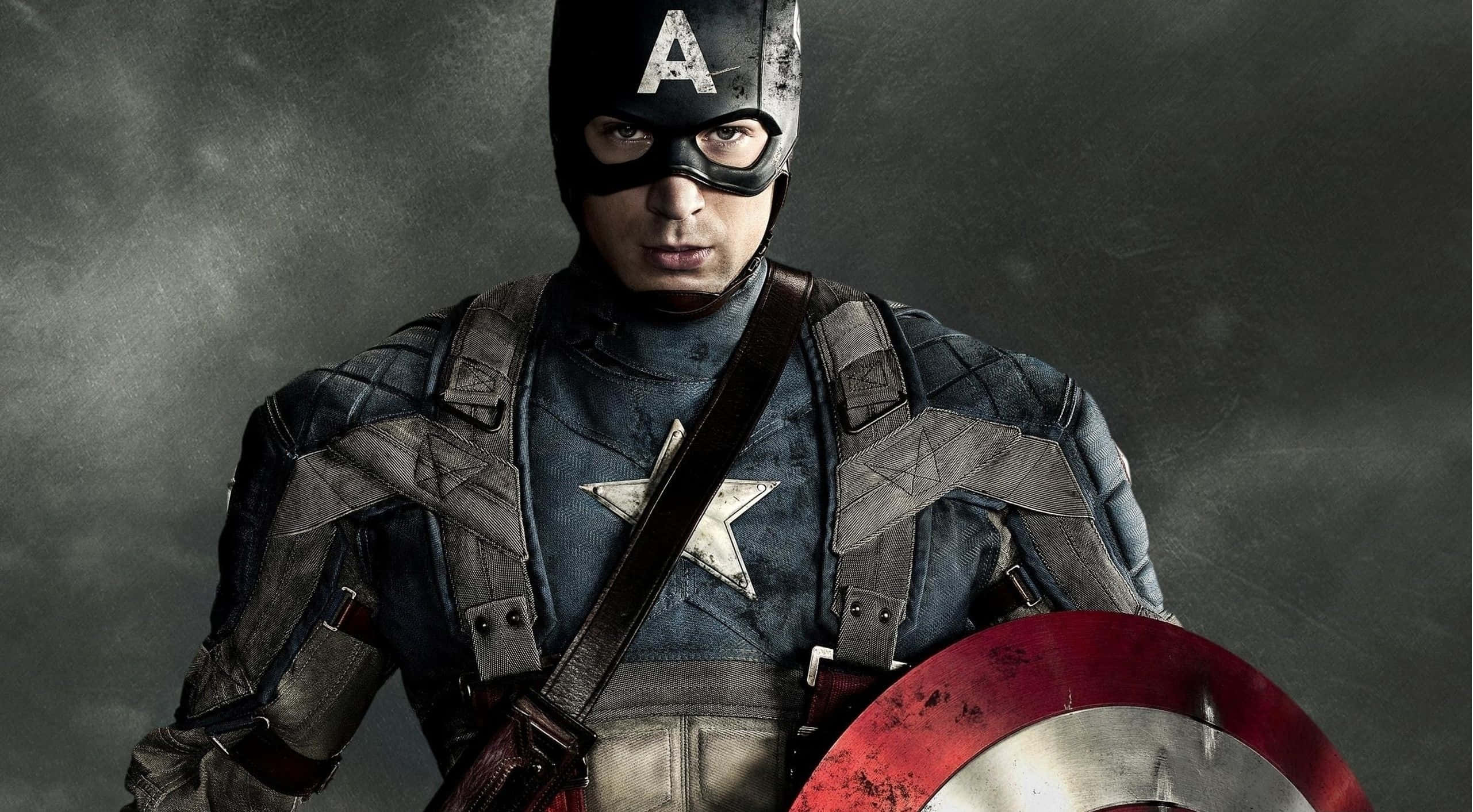 Best Captain America 桌布 壁紙 — 美國隊長身穿破舊制服，在暴風雨般的灰色背景下堅定地握著他標誌性的盾牌。