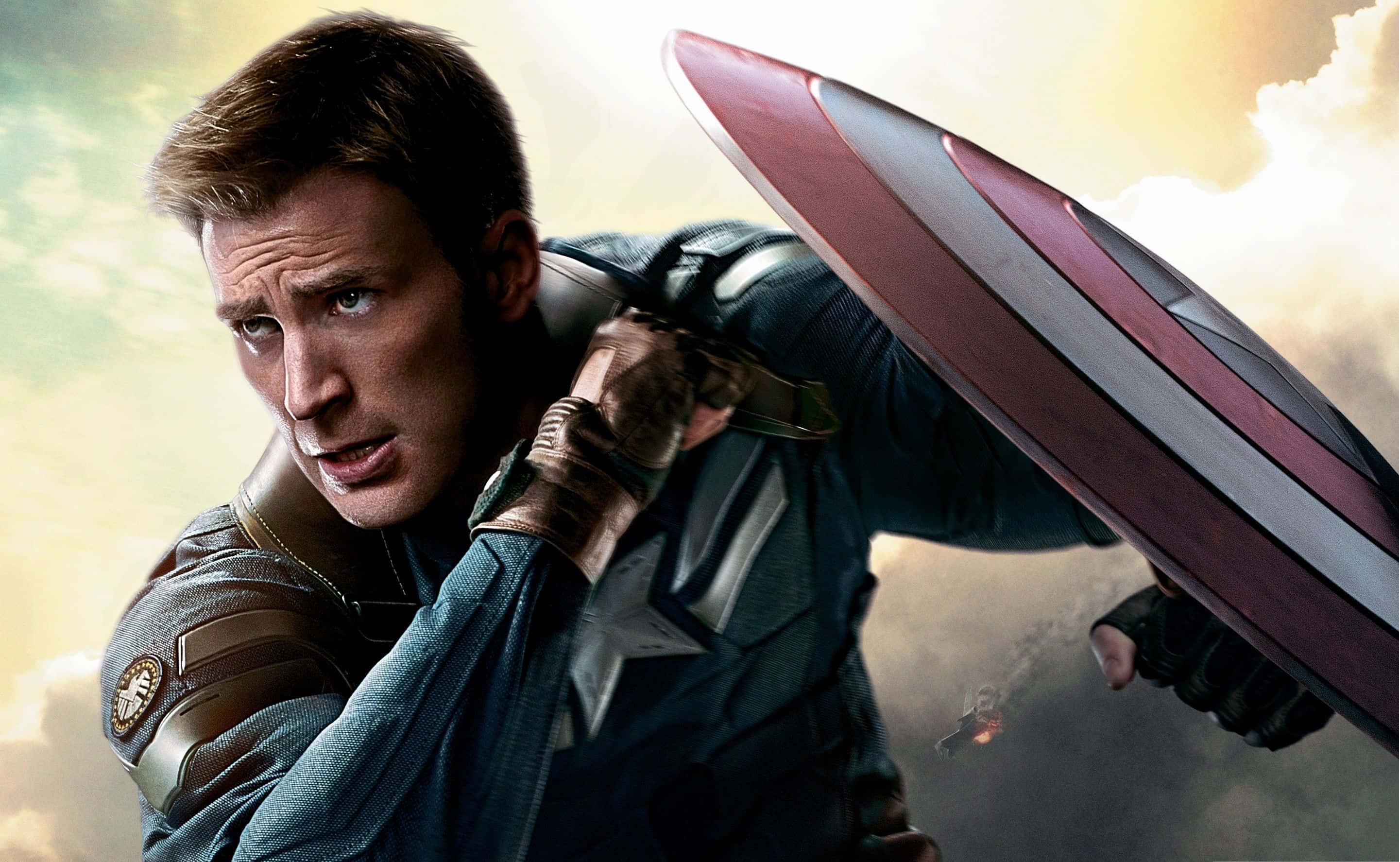 Best Captain America 桌布 壁紙 — 美國隊長身穿藍色制服，在陰雲密布的天空下以動態戰鬥姿勢手持標誌性的紅、白、藍盾牌。