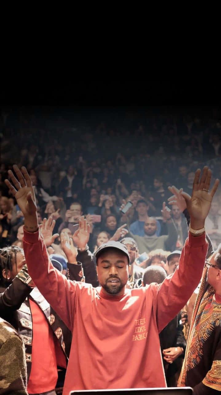 美國音樂人坎耶·威斯特在《The Life Of Pablo》巡迴演唱會上演出 壁紙 — Kanye West 在演唱會中於舞台燈光和煙霧中舉起雙手，身處人群之中。