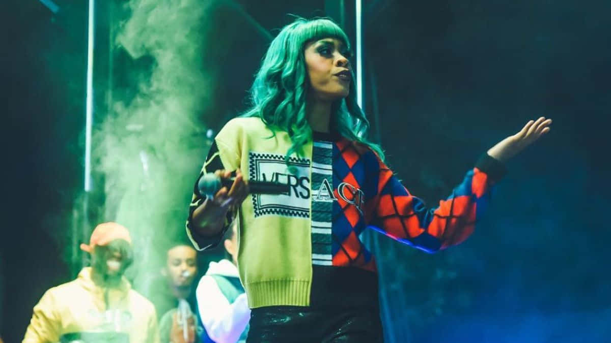 綠髮歌手在霓虹燈舞台上與伴舞一同表演。