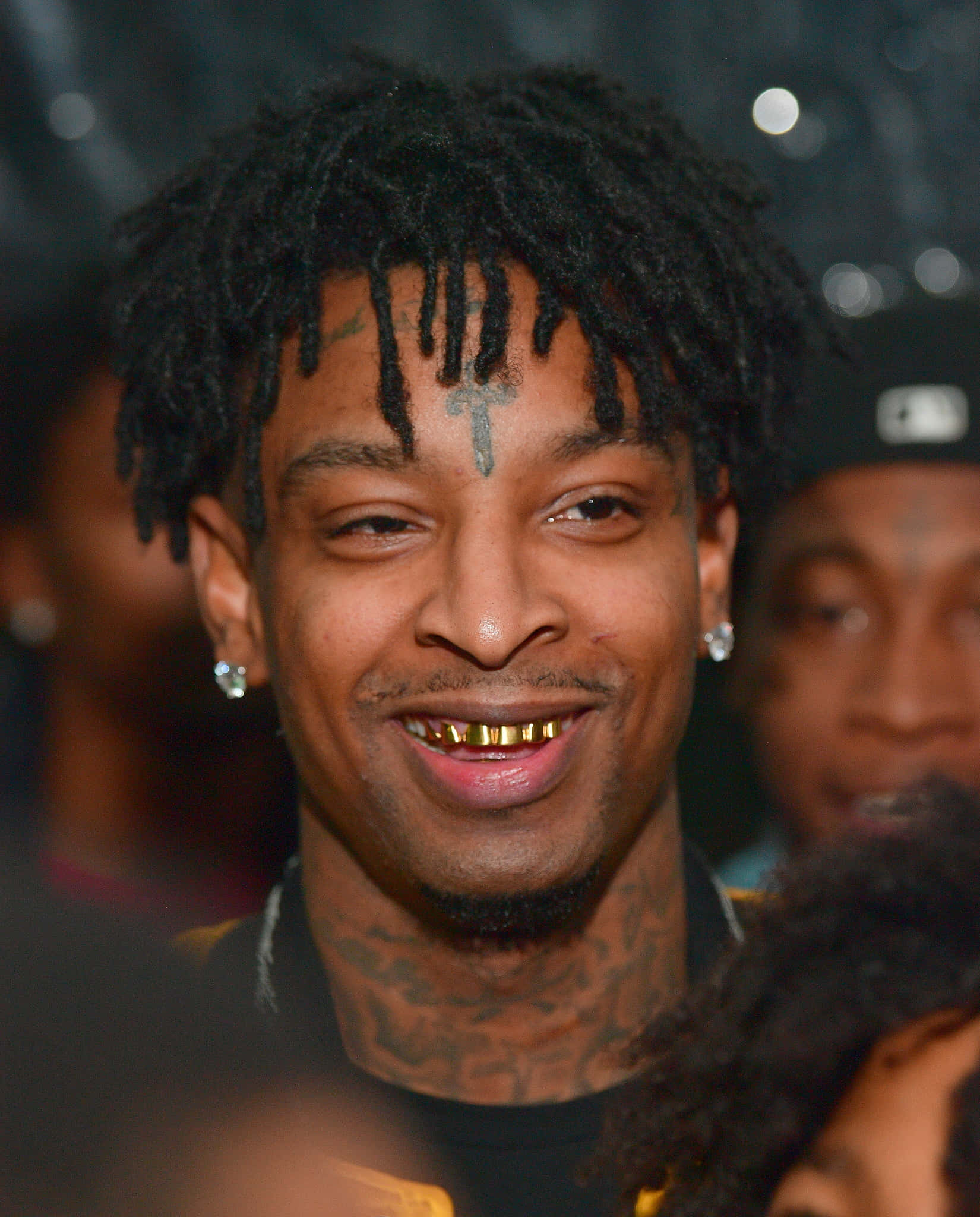 美國饒舌歌手21 Savage 壁紙 — 一個微笑男子的特寫肖像，他有辮子頭、金牙套，額頭上有一個十字架紋身。