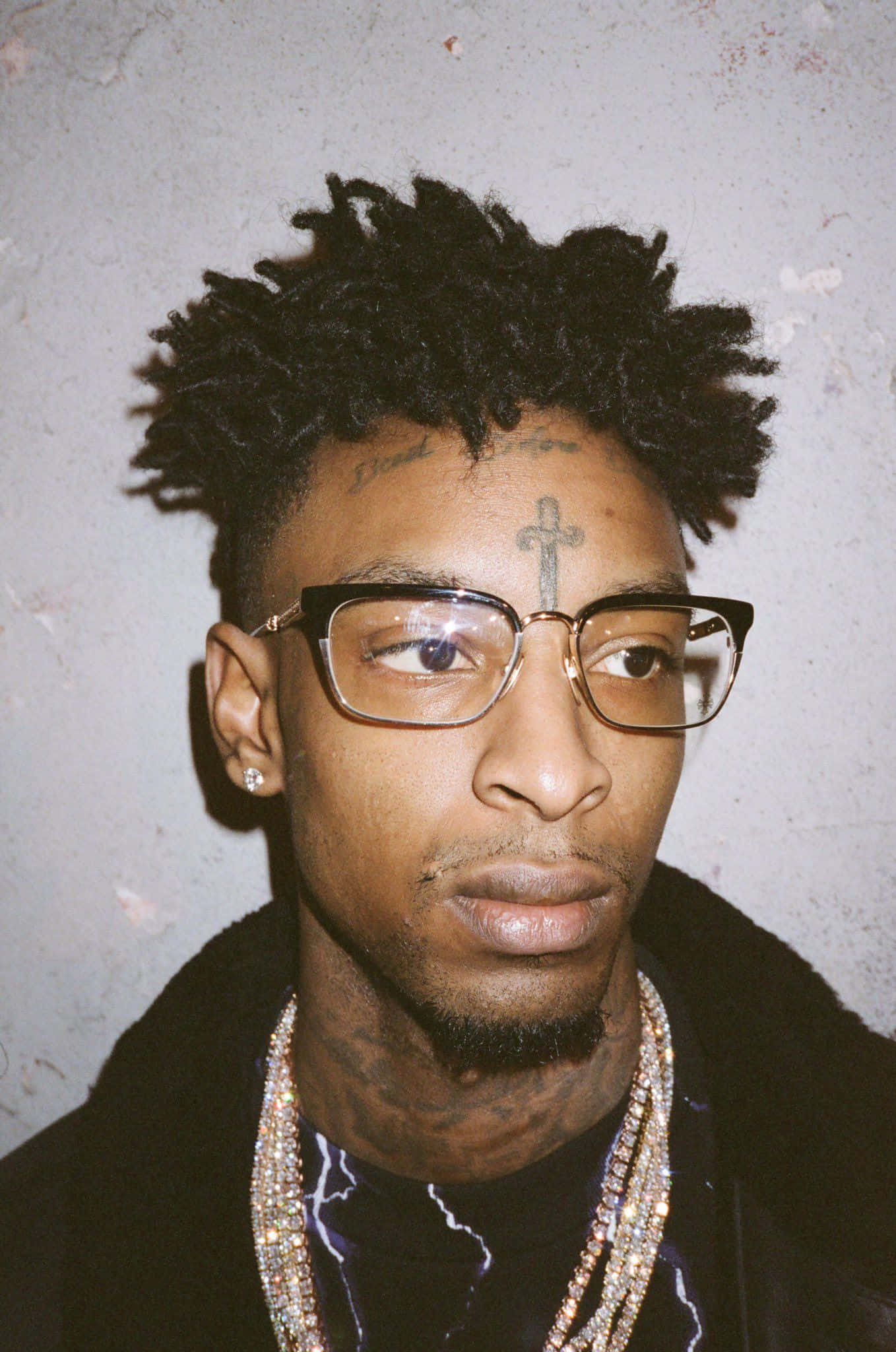 美國饒舌歌手兼作曲人 21 Savage 壁紙 — 一個男人嘅特寫肖像，佢有辮子頭同眼鏡，背景係有紋理嘅灰色牆。