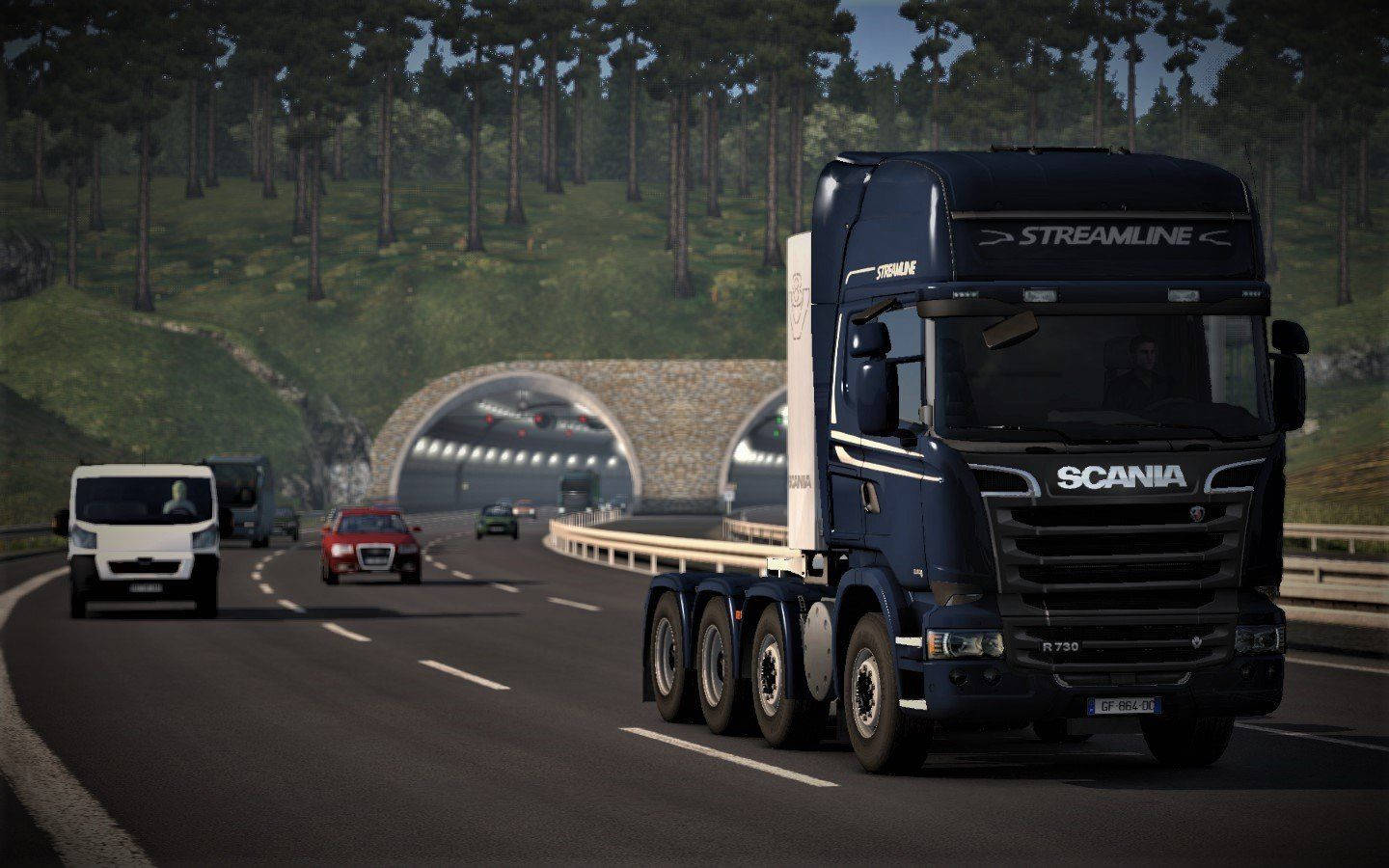 藍色 Scania 貨車在山區高速公路上駛向隧道，背景為森林。