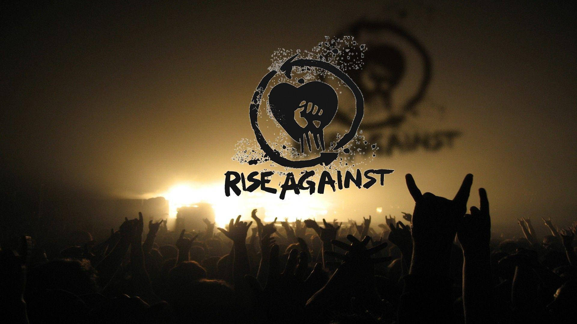 美國龐克搖滾樂隊 Rise Against 壁紙 — 剪影的演唱會人群在溫暖的舞台燈光下舉起雙手，'Rise Against' 標誌在煙霧中發光。