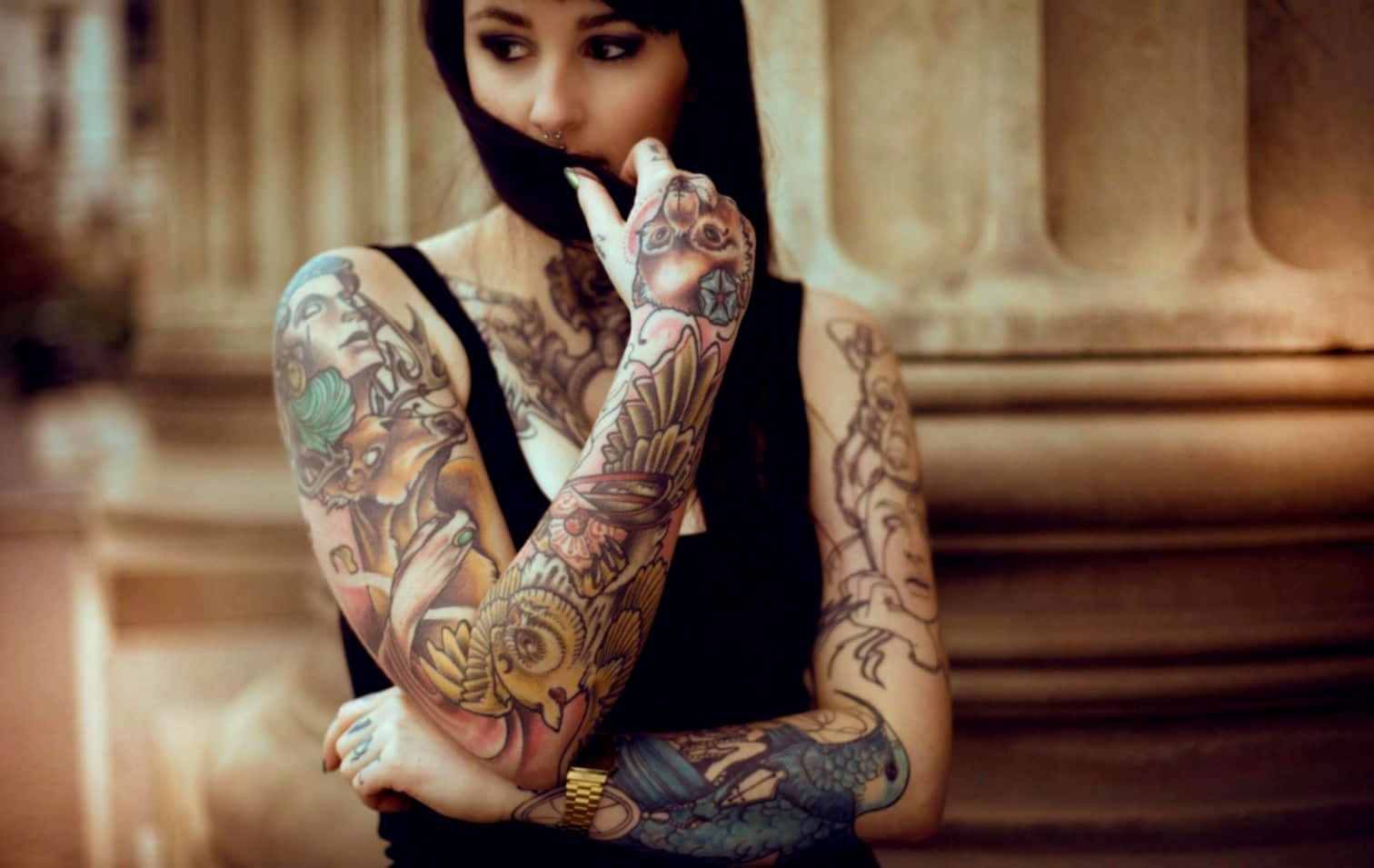 美在內心 壁紙 — 一位擁有複雜彩色紋身的女性，在經典石柱背景下遮住嘴巴。