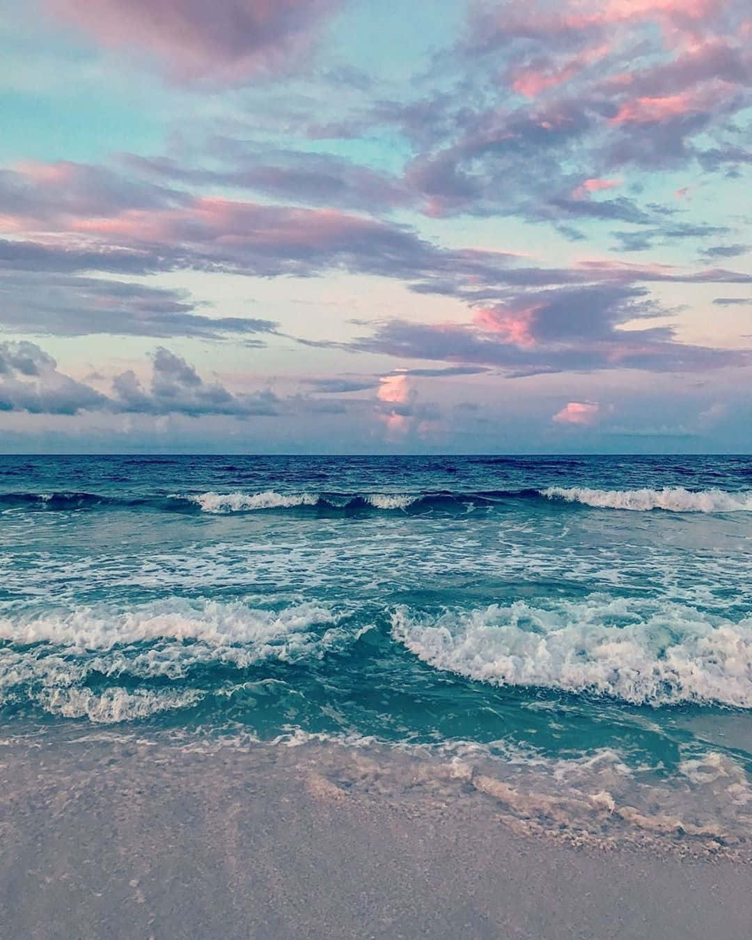 美學 Instagram 天空與海洋 壁紙 — 在粉彩粉紅和藍色的日落天空下，碧綠色的海浪拍打著沙灘。