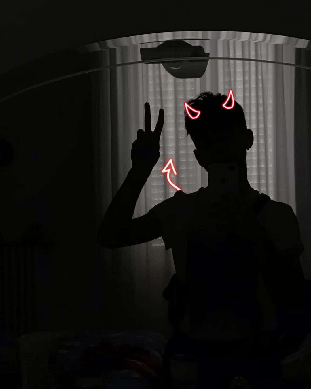 在黑暗房間的鏡子自拍中，帶有發光紅色惡魔角和和平手勢的人物剪影。