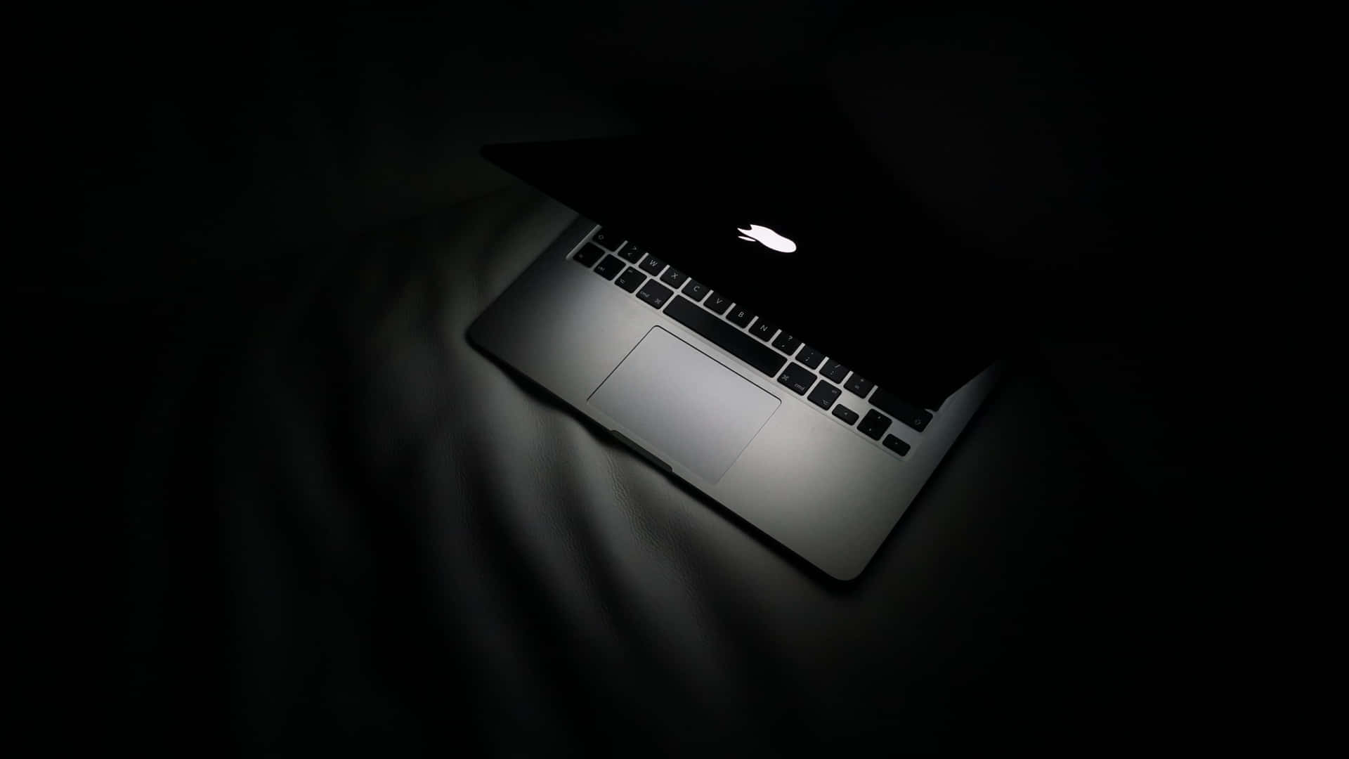 在昏暗房間的深色織物上發光的筆記型電腦。