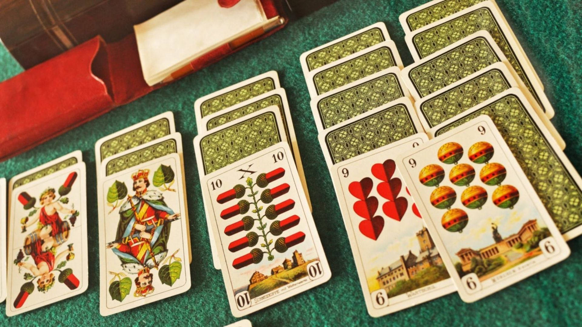 美學 Solitaire 撲克牌 壁紙 — 復古撲克牌，帶有華麗插圖和綠色圖案背面，在綠色氈面上呈扇形展開。