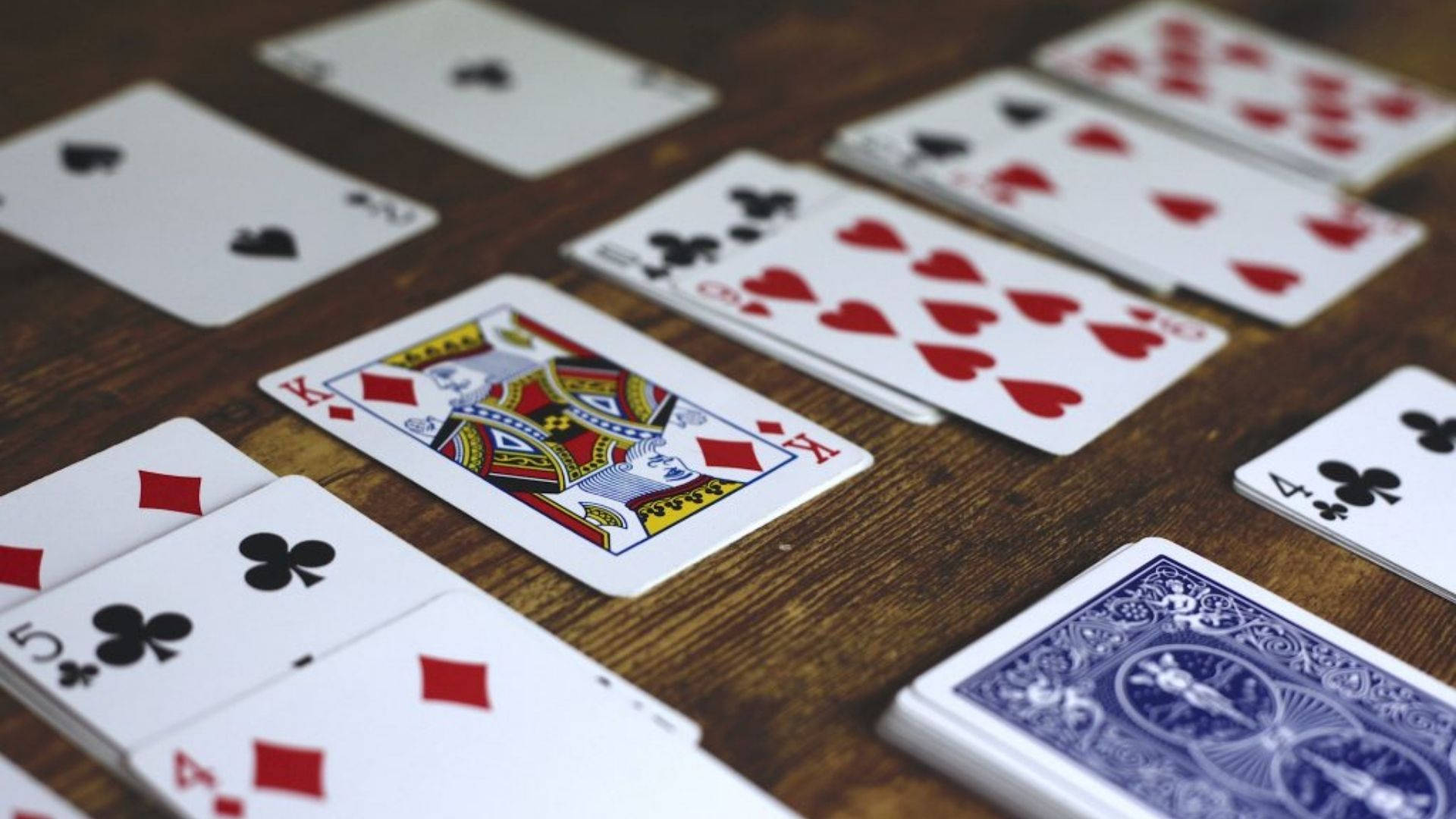 美學Solitaire遊戲 壁紙 — 特寫鏡頭：散落嘅啤牌喺鄉村風格木枱上，配以溫暖燈光。