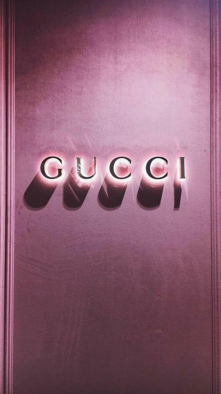 美學Tumblr Gucci燈光 壁紙 — 發光的Gucci標誌以粗體字母在紋理灰紫色牆壁上投射出戲劇性的陰影，牆壁由優雅的線板框起。