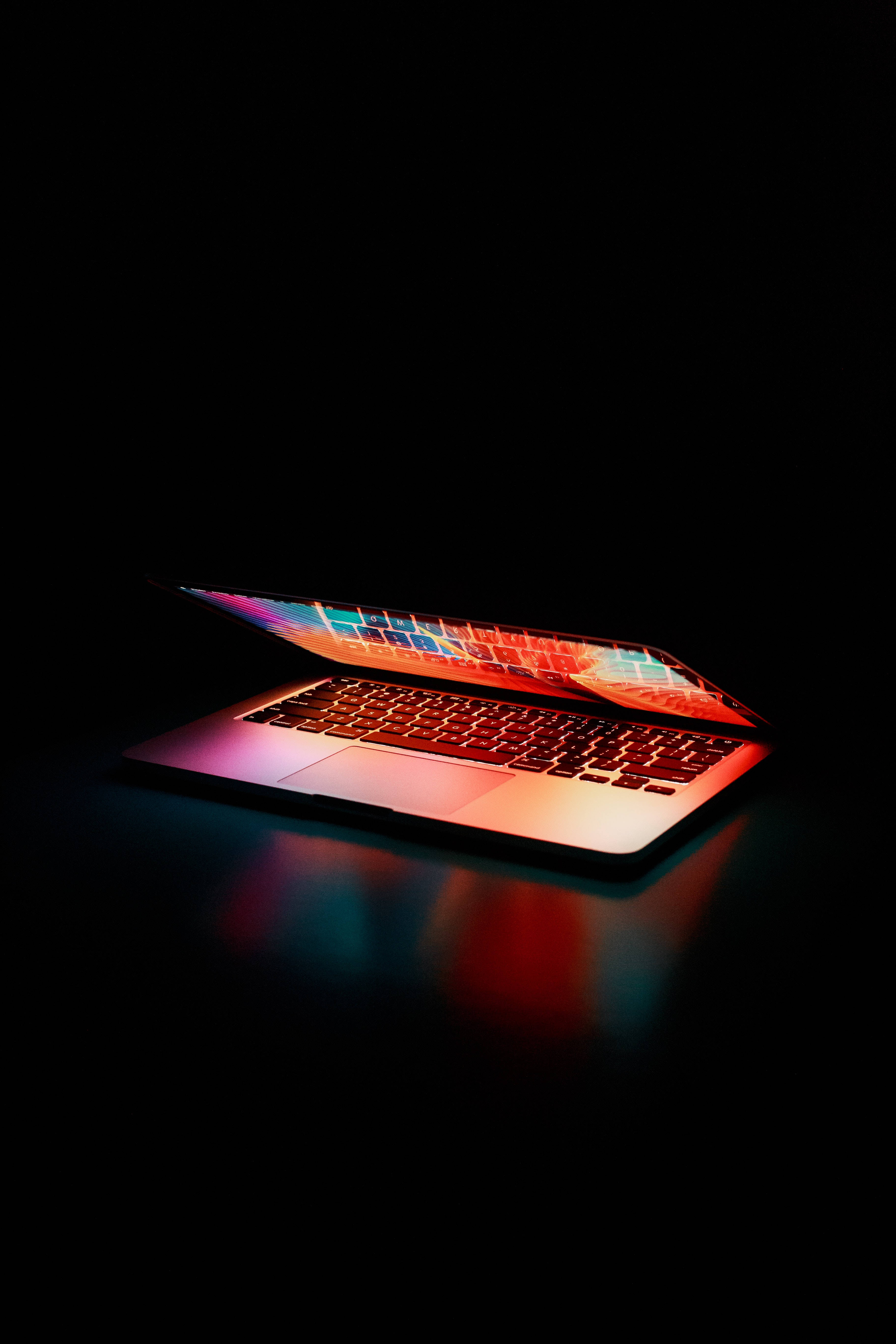 美學Tumblr筆記本AMOLED 壁紙 — 一部時尚的筆記型電腦在黑色背景的暗色表面上散發出鮮豔的霓虹反射光芒。