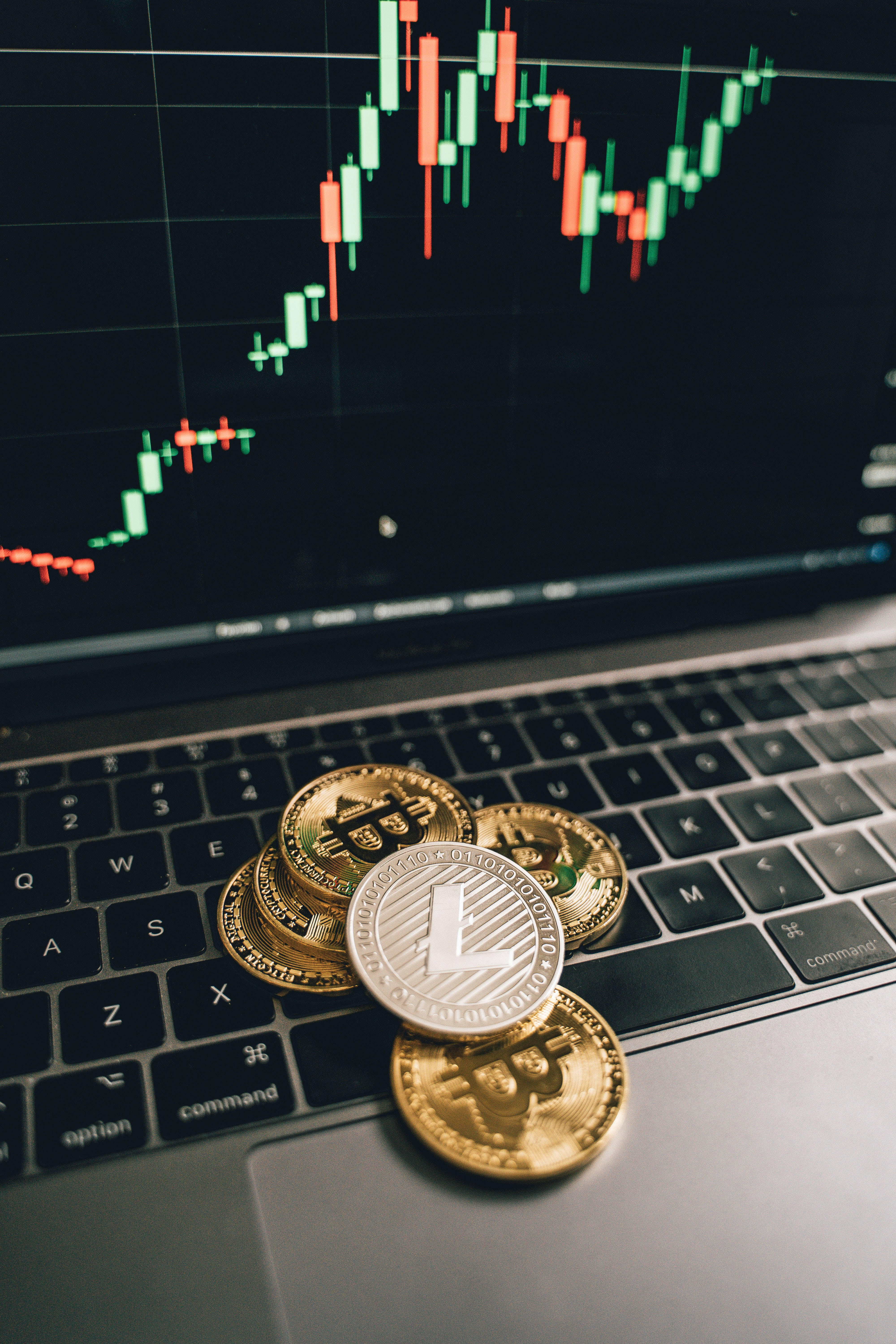 美學Tumblr筆電比特幣 壁紙 — 金色萊特幣硬幣放在筆記型電腦鍵盤上，螢幕上顯示發光的加密貨幣交易圖表。