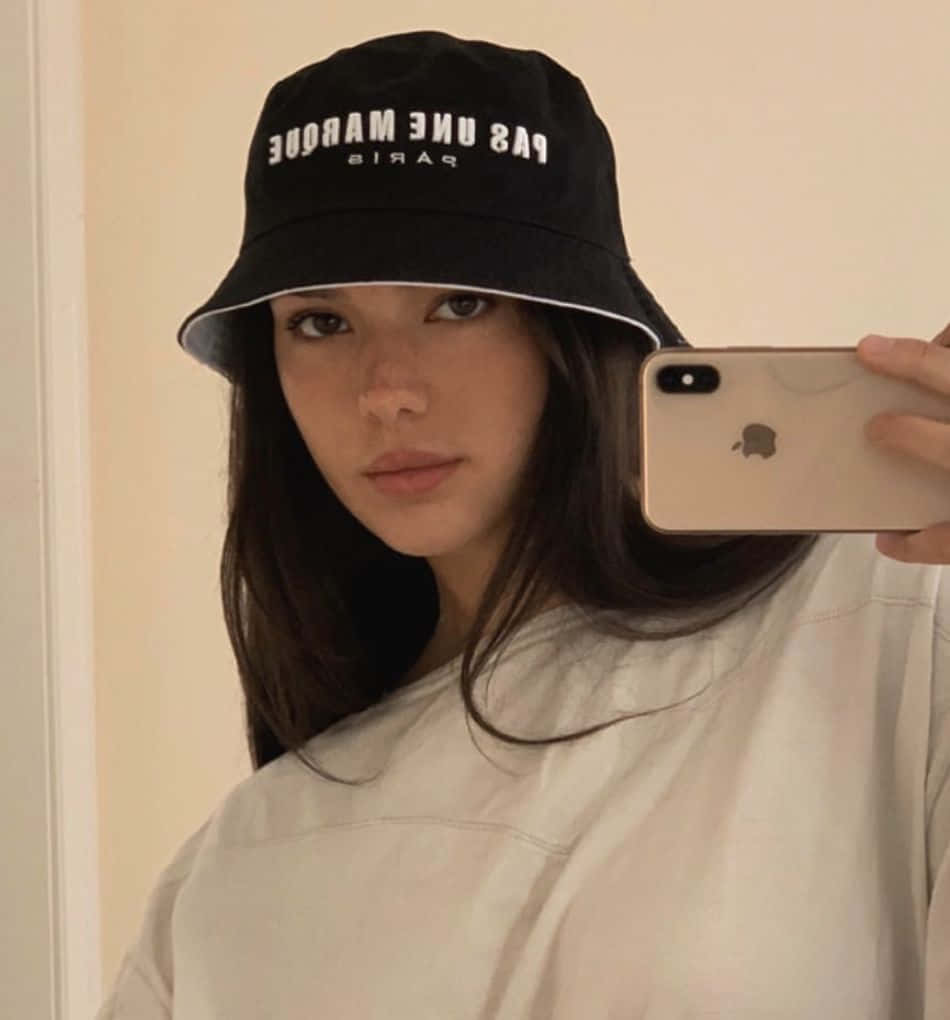 年輕女性戴著黑色漁夫帽和白色襯衫對著鏡子自拍。