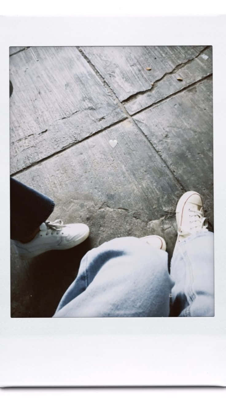 兩個人穿著牛仔褲和白色運動鞋坐在裂開的路面上，有一個畫出來的心形。 — 寶麗來 GIF 壁紙