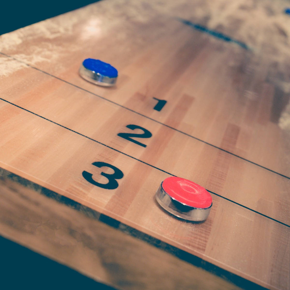 美學復古 Shuffleboard 遊戲與球 壁紙 — 紅色和藍色沙狐球圓盤的特寫，放置在帶有編號得分線的木製球場上。