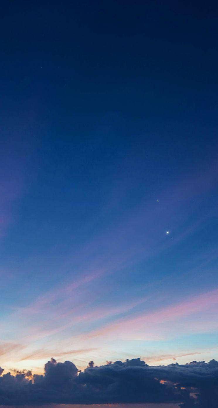 美學手機多雲藍天背景 壁紙 — 寧靜的暮色天空，在暗雲和遠處閃爍的星星之上，有柔和的粉紅色和藍色漸變。