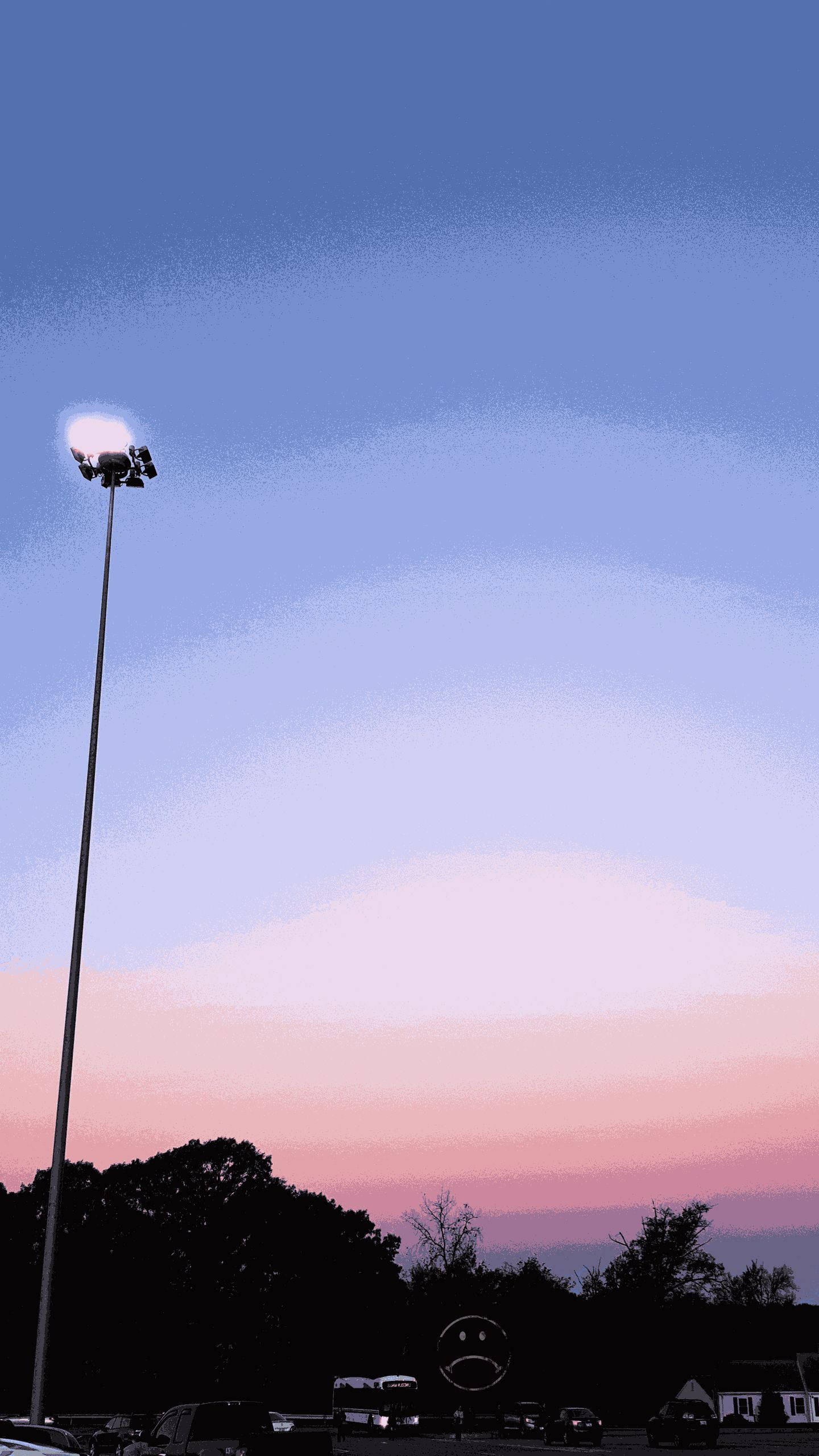 美學手機燈柱背景 壁紙 — 一支高大的體育場燈柱矗立在暮色天空下，天空塗上柔和的粉紅和藍色調，上方是黑暗的樹線和停泊的汽車。