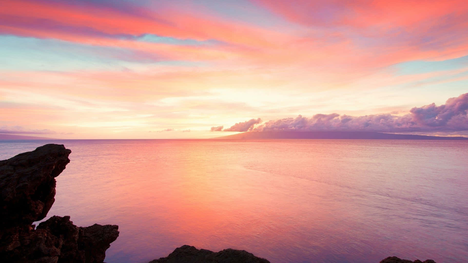 美學淡彩夕陽海景背景 壁紙 — 寧靜的日落，平靜的海面上有鮮豔的粉紅色、橙色和紫色雲彩，下方是黑暗的岩石前景。