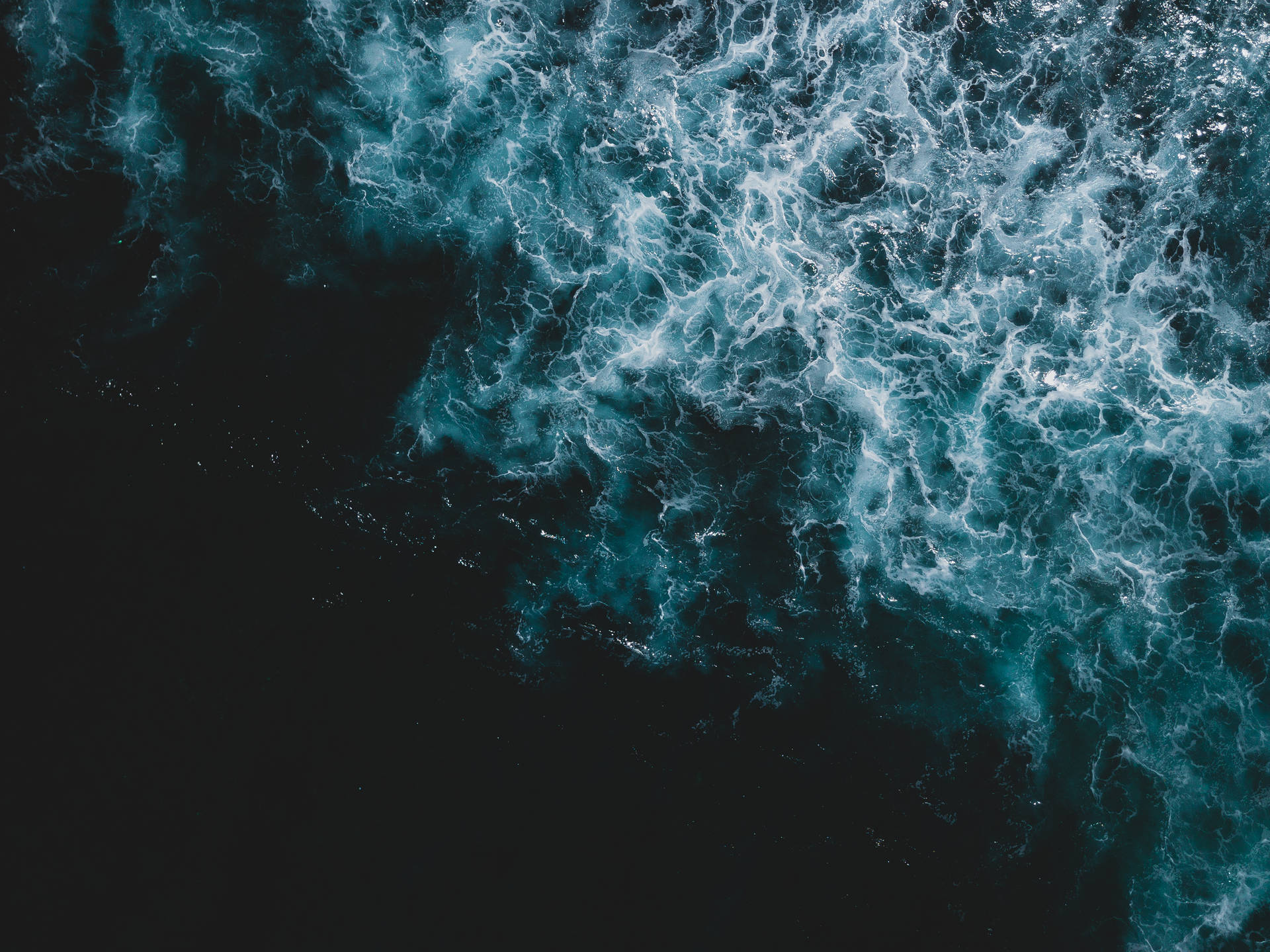 從空中俯瞰海浪破碎，白色泡沫與黑暗海水形成對比。
