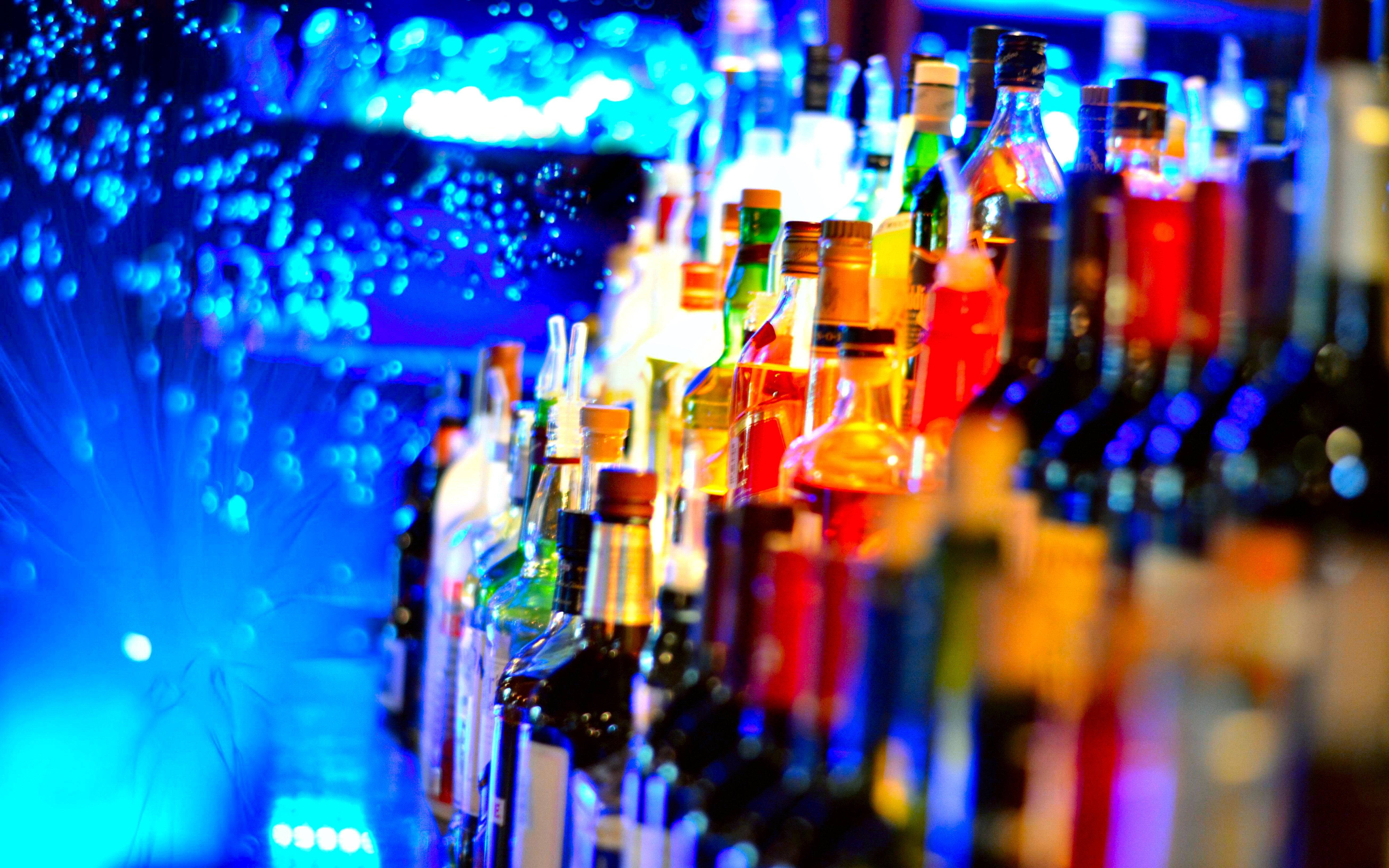 美學酒吧飲品 壁紙 — 一排排色彩繽紛的酒瓶在昏暗的酒吧中，在充滿活力的藍色霓虹燈下閃耀。