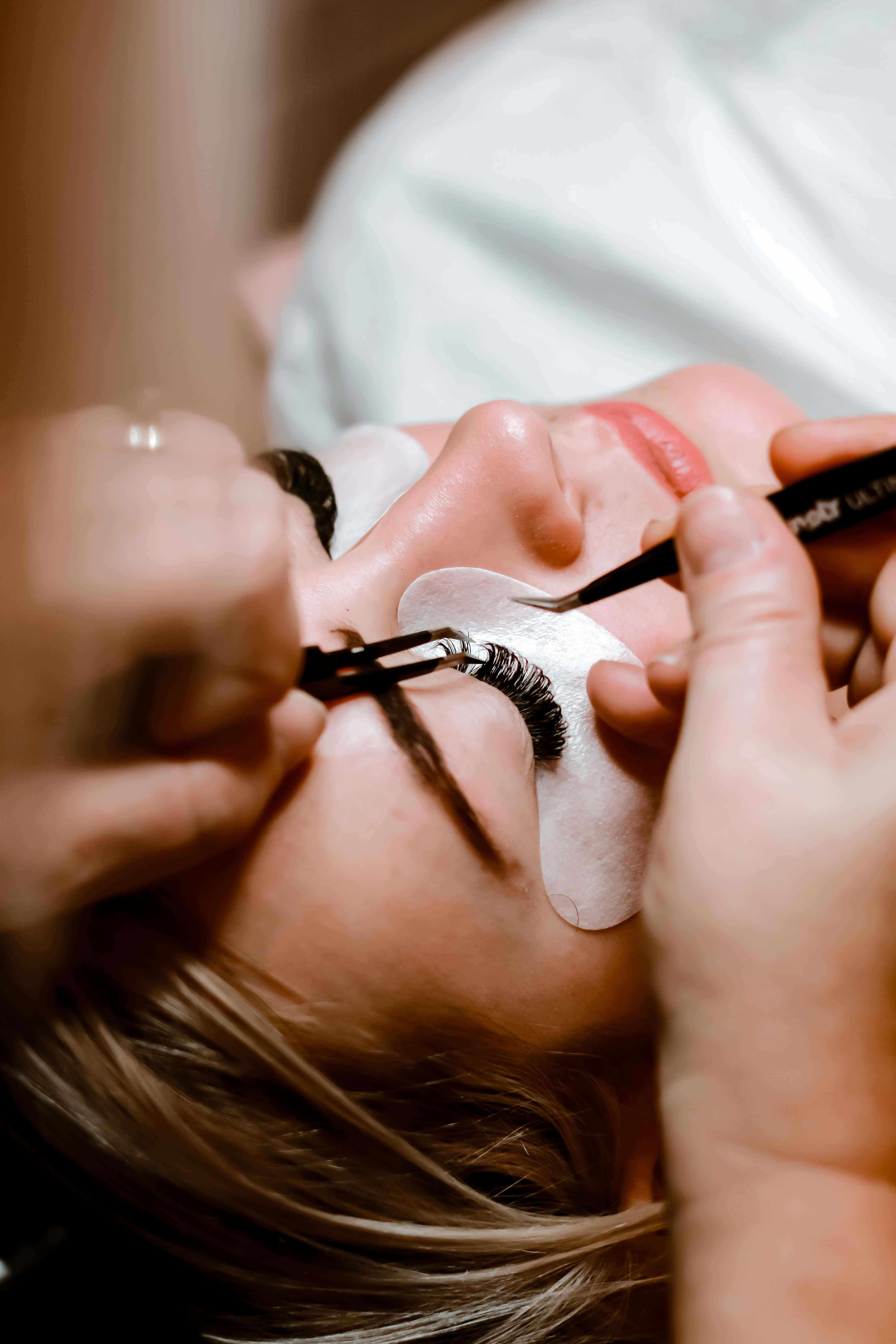 Beauty Salon 桌布 壁紙 — 美容院中，一個人正在用鑷子和睫毛刷貼假眼睫毛的特寫。
