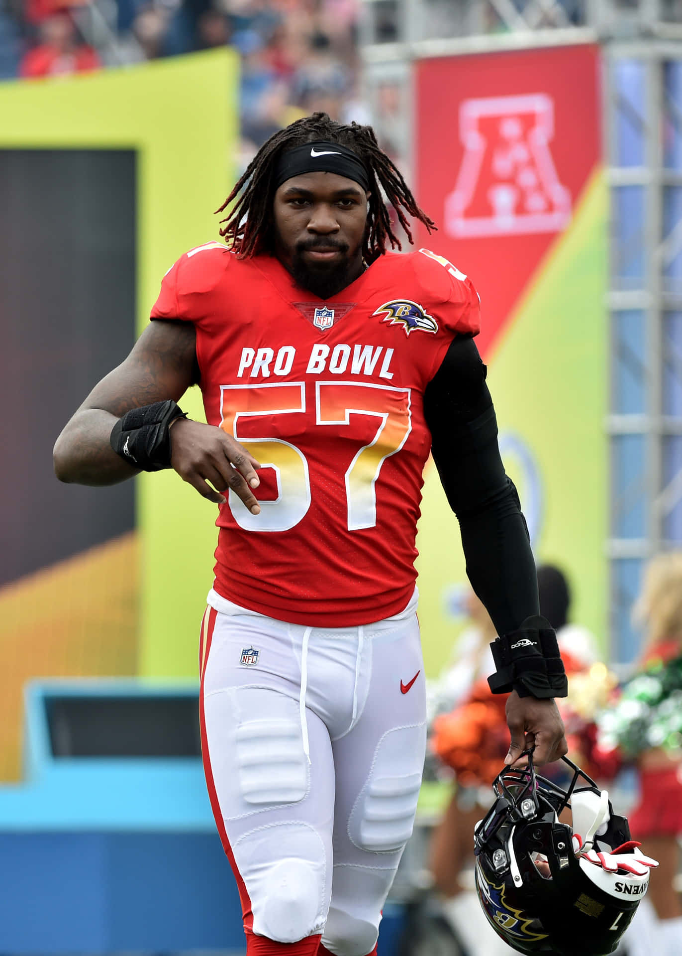 身穿紅色Pro Bowl球衣的足球員在體育場手持頭盔行走。