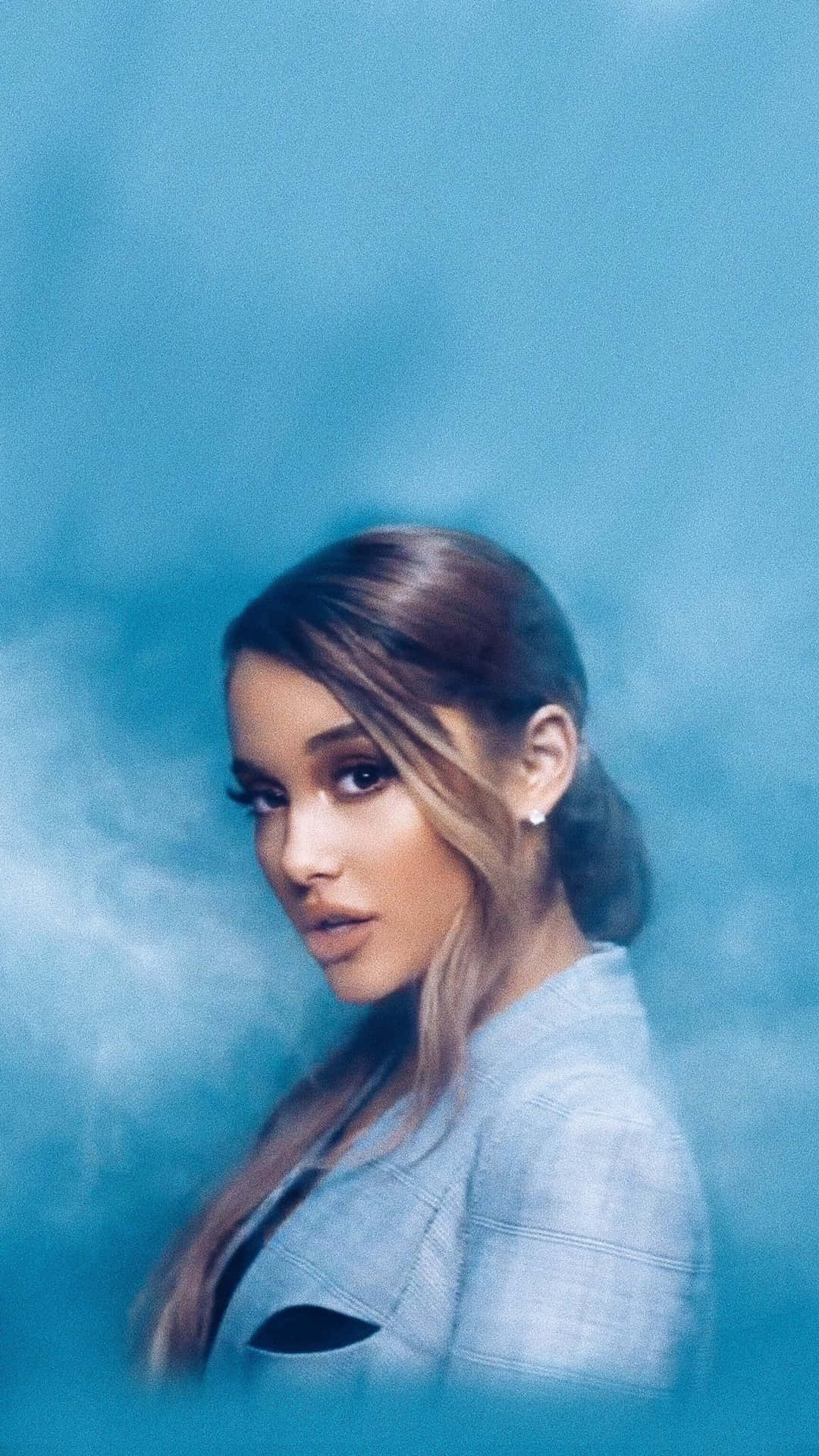Ariana Grande 身穿淺藍色西裝外套，背景係煙霧瀰漫嘅藍色。