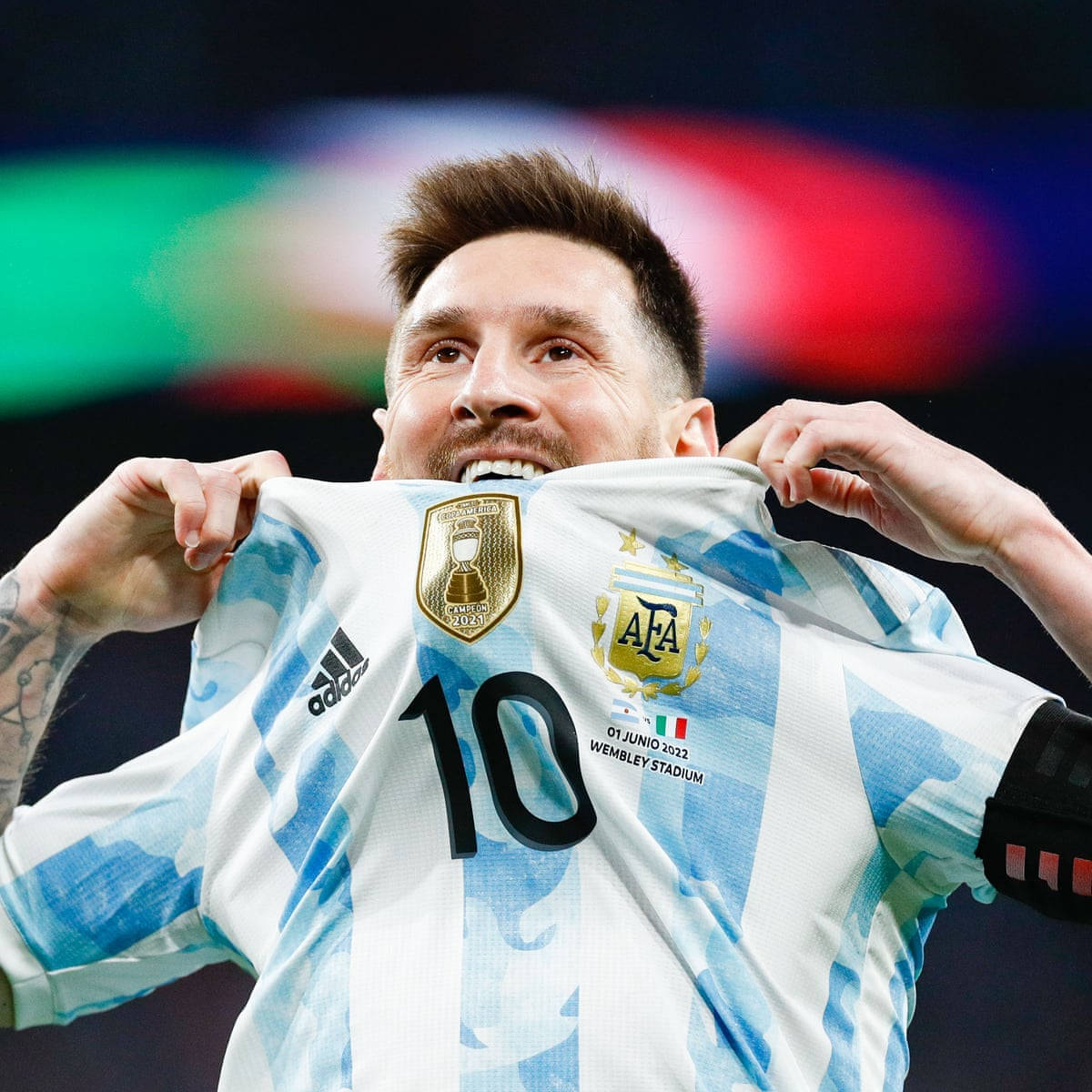 Argentina National Football Team 桌布 壁紙 — 美斯在溫布萊球場高舉帶有2022年世界盃臂章的阿根廷球衣，露出勝利的笑容。