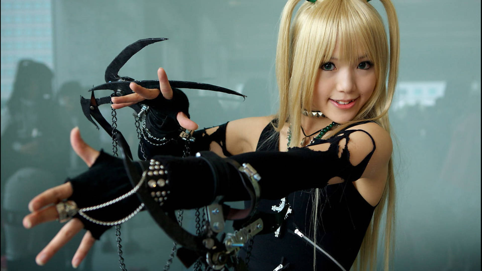 美沙·阿曼可愛Cosplay 壁紙 — 一位微笑的金髮女性身穿黑色哥德式cosplay，自信地揮舞著一把華麗的大型爪狀武器。