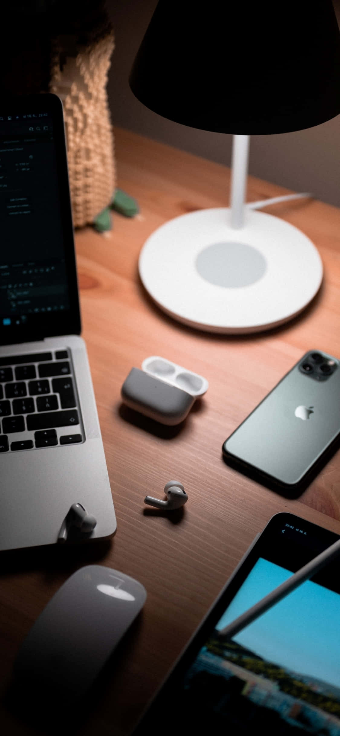 美觀工作空間：iPhone X 置於現代木質書桌 壁紙 — 溫暖照明的木桌上放有手提電腦、手機、耳塞和燈，營造出舒適的科技工作空間氛圍。