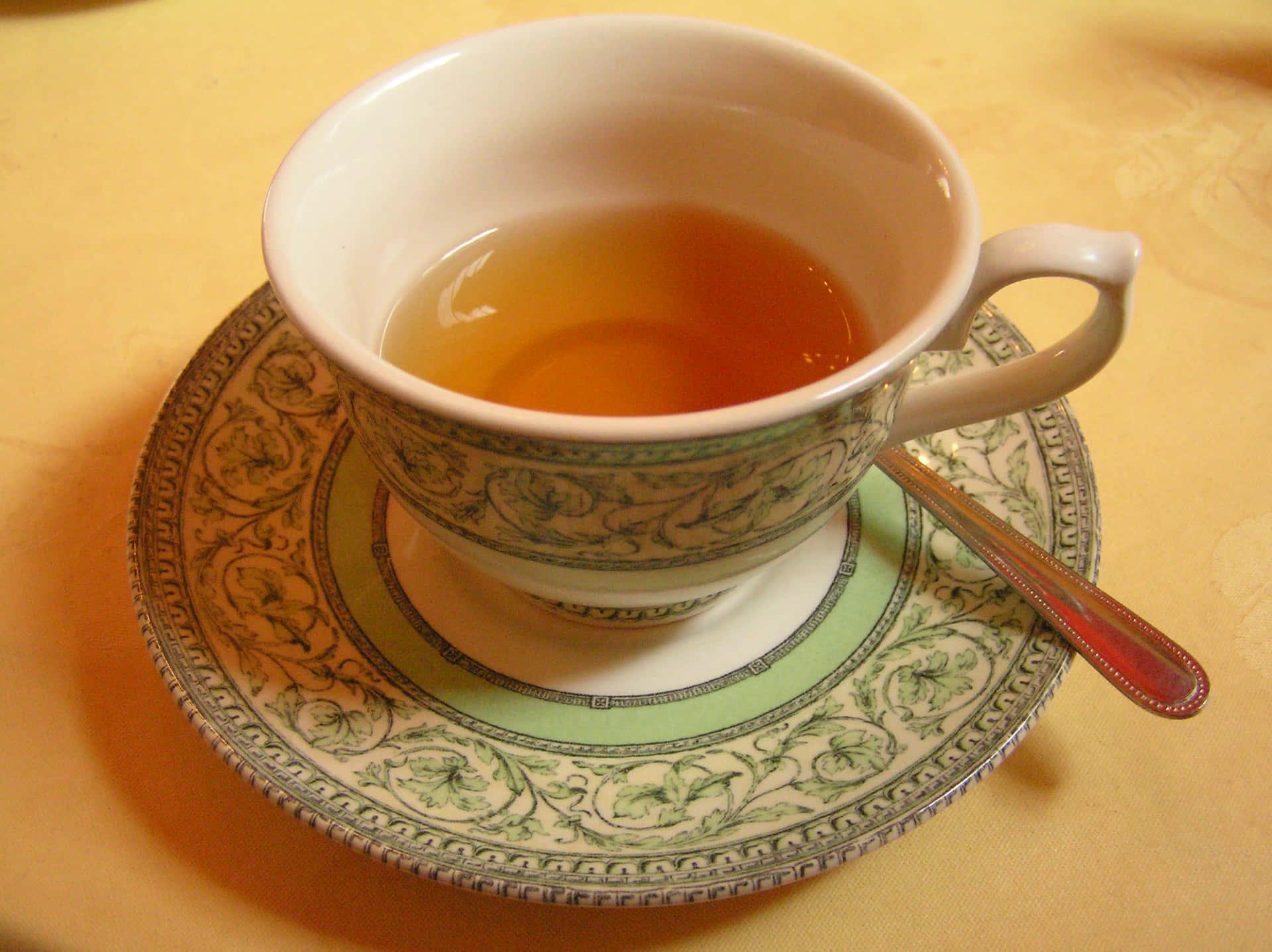 一個華麗的茶杯盛滿琥珀色茶，放在茶托上，配有一把銀匙，置於金色桌布上。