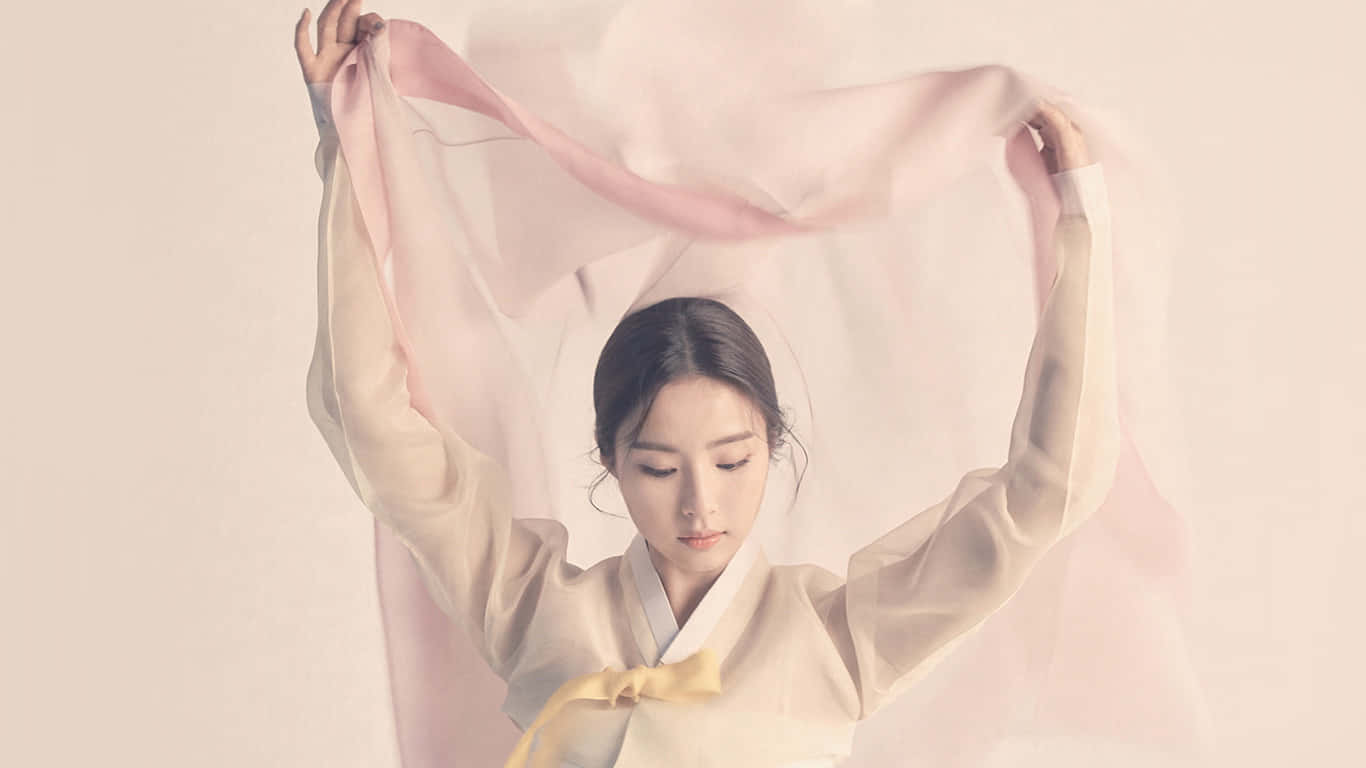 美麗亞洲女演員身著韓服 壁紙 — 一位穿著傳統服飾的寧靜女性，在柔和的純色背景下優雅地舉起一條飄逸的粉紅色絲巾。