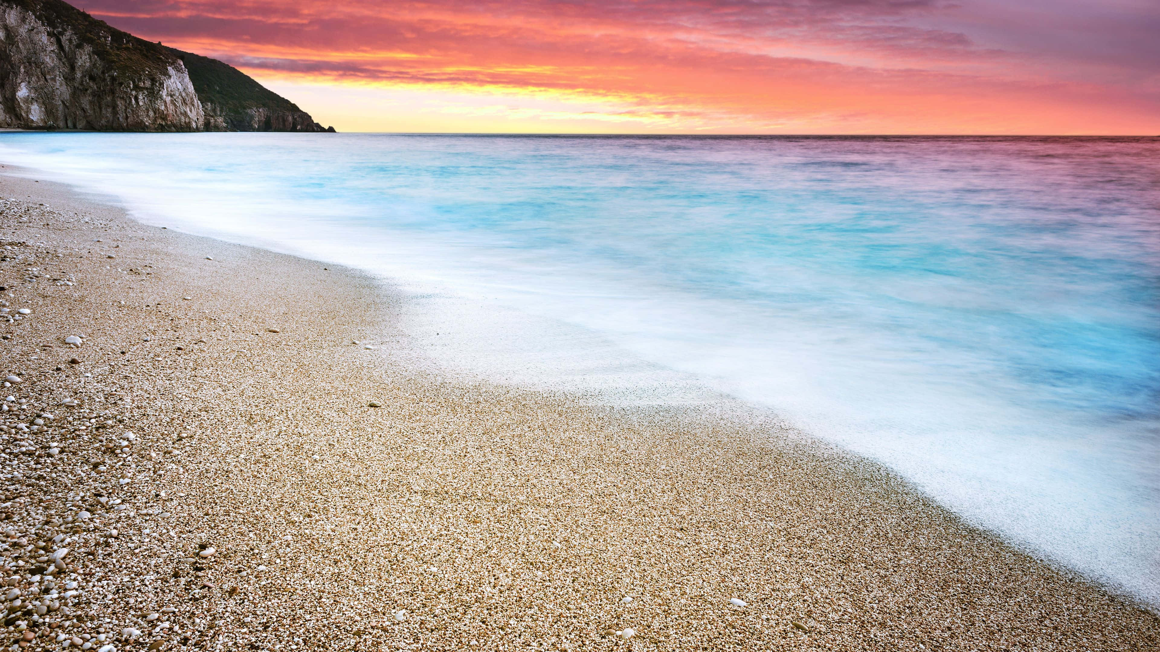 美麗傍晚的海灘日落 壁紙 — 夕陽下寧靜的海灘，柔和的海浪拍打著金色沙灘，天空呈現火熱的橙色和粉紅色。