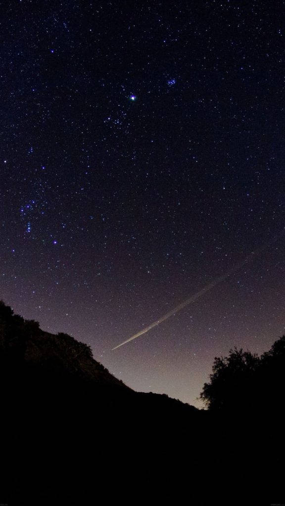 美麗夜空中的流星 壁紙 — 一顆明亮的流星劃過繁星點點的夜空，下方是黑暗的山丘和樹木剪影。
