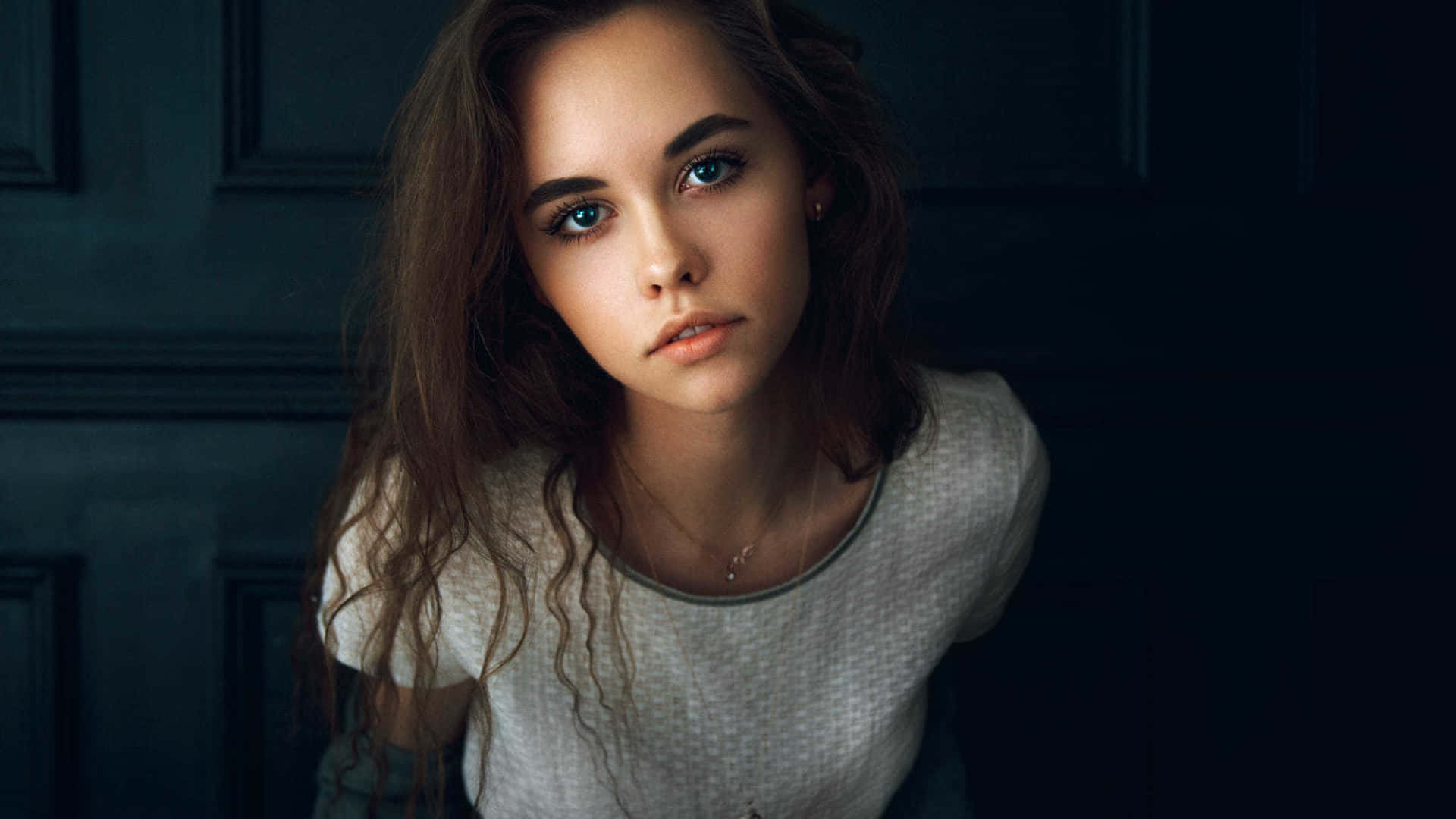 美麗少女寫真 壁紙 — 一位擁有引人注目的藍色眼睛和波浪棕色頭髮的年輕女性，在深色鑲板門背景下凝視著。