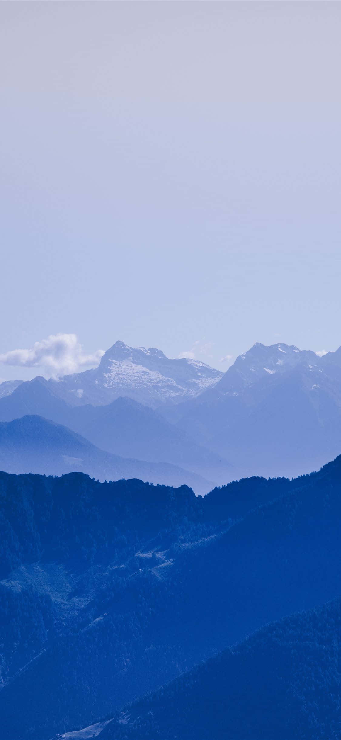 美麗山景藍色漸層背景 壁紙 — 寧靜的山脈，白雪覆蓋的山峰在柔和日光下漸漸融入朦朧的藍天。