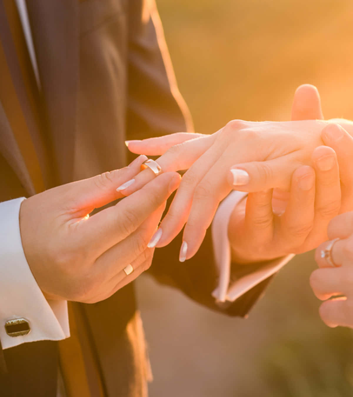 新郎在金色陽光下將結婚戒指戴在新娘的手指上。