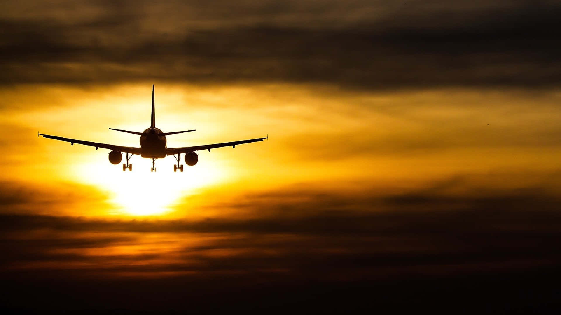 美麗日落降落飛機背景 壁紙 — 一架商用飛機在熾熱的日落天空和發光的雲層襯托下形成剪影。