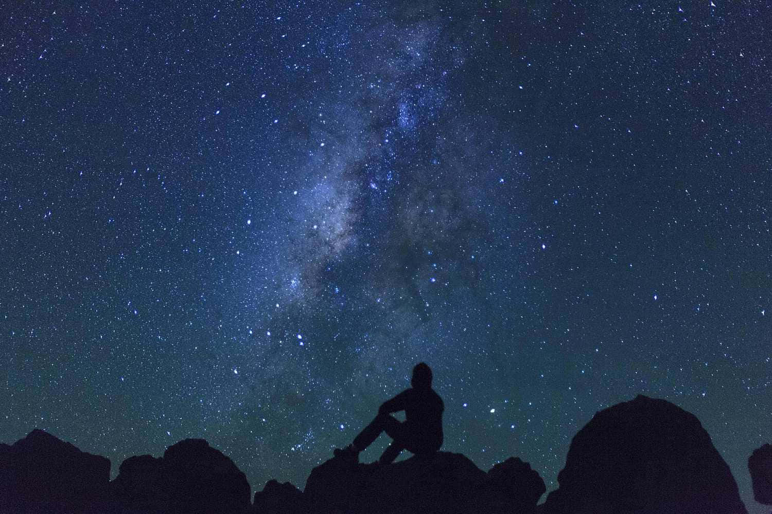 美麗星空天文攝影 壁紙 — 一個孤獨的身影坐在岩石地形上，仰望充滿銀河閃耀帶的壯麗星空。