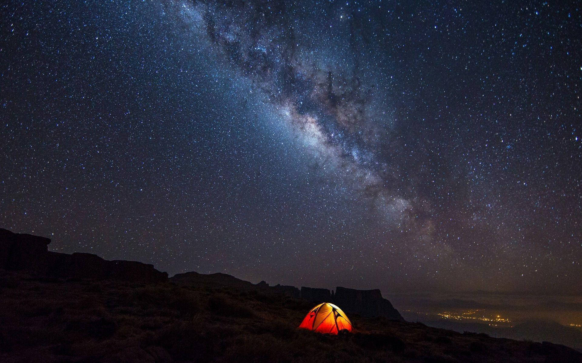 一個發光的橙色帳篷在星空下，銀河可見。