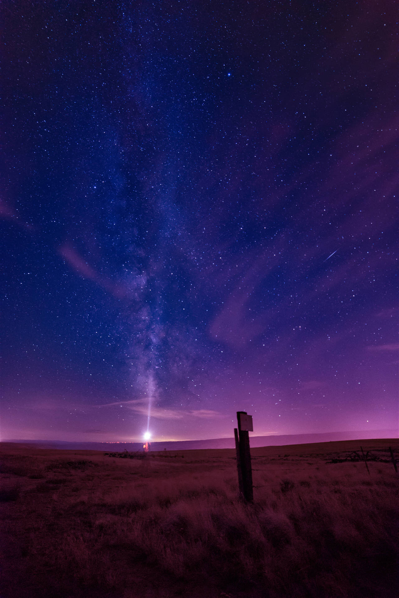 繁星點點的夜空，銀河在沙漠景觀和遠處燈光上空。