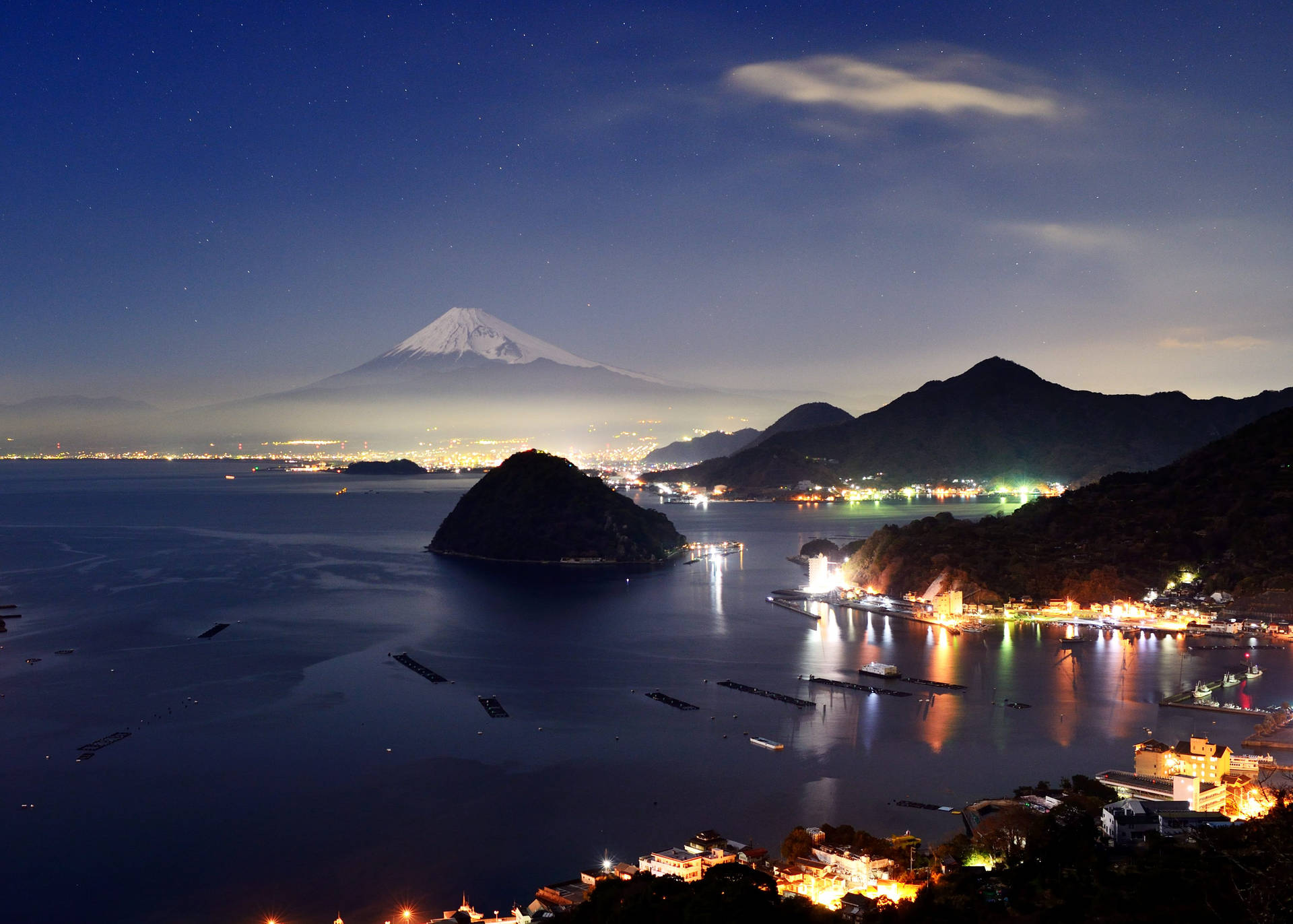 夜晚的富士山，發光的沿海城鎮和星空倒映在平靜的水面上。