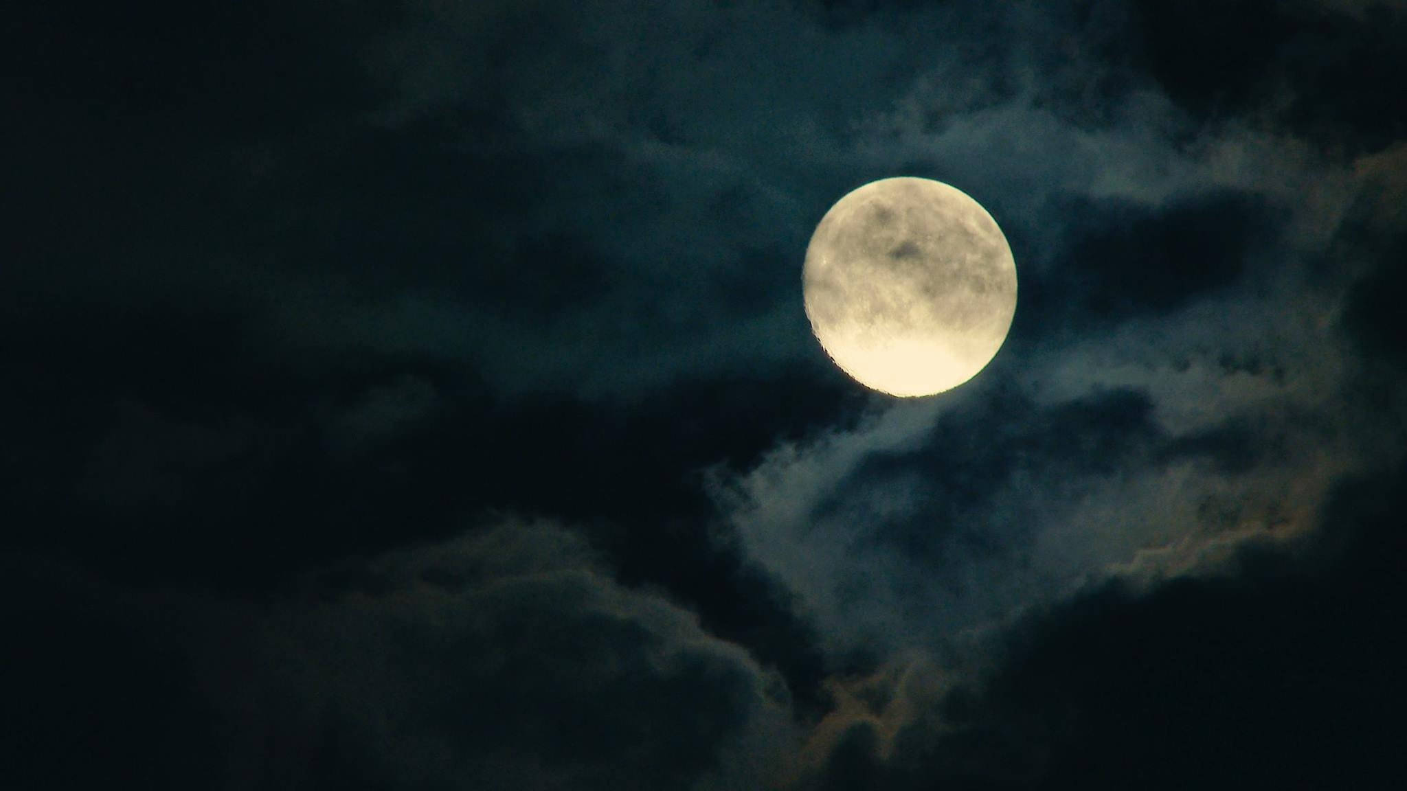 美麗滿月與夜空雲朵 壁紙 — 一輪明亮的滿月穿過旋轉的烏雲，在陰鬱的夜空中閃耀。