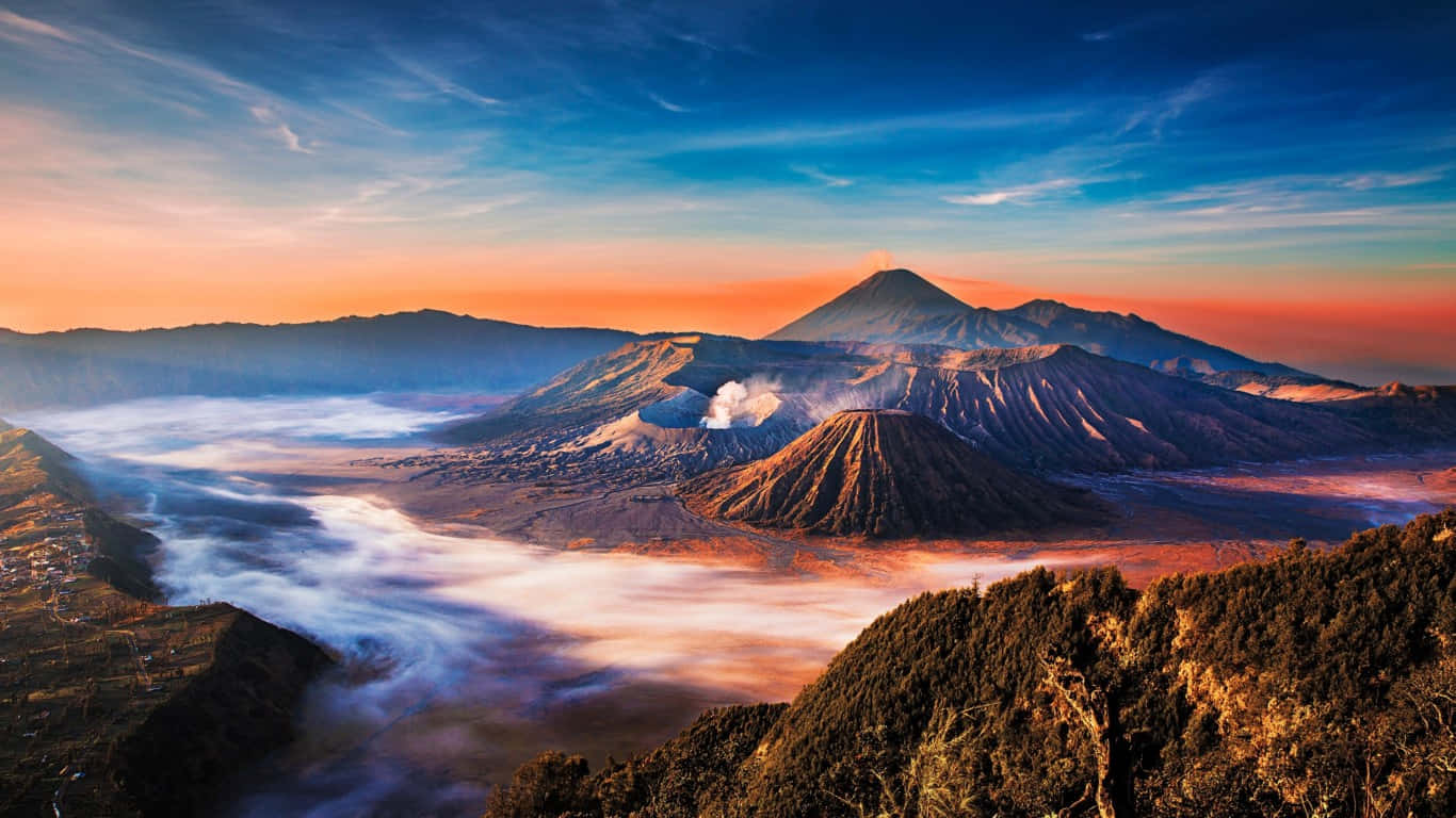 日出時分的火山山脈，薄霧流過山谷，山峰在溫暖的橙色和涼爽的藍色調中閃耀。