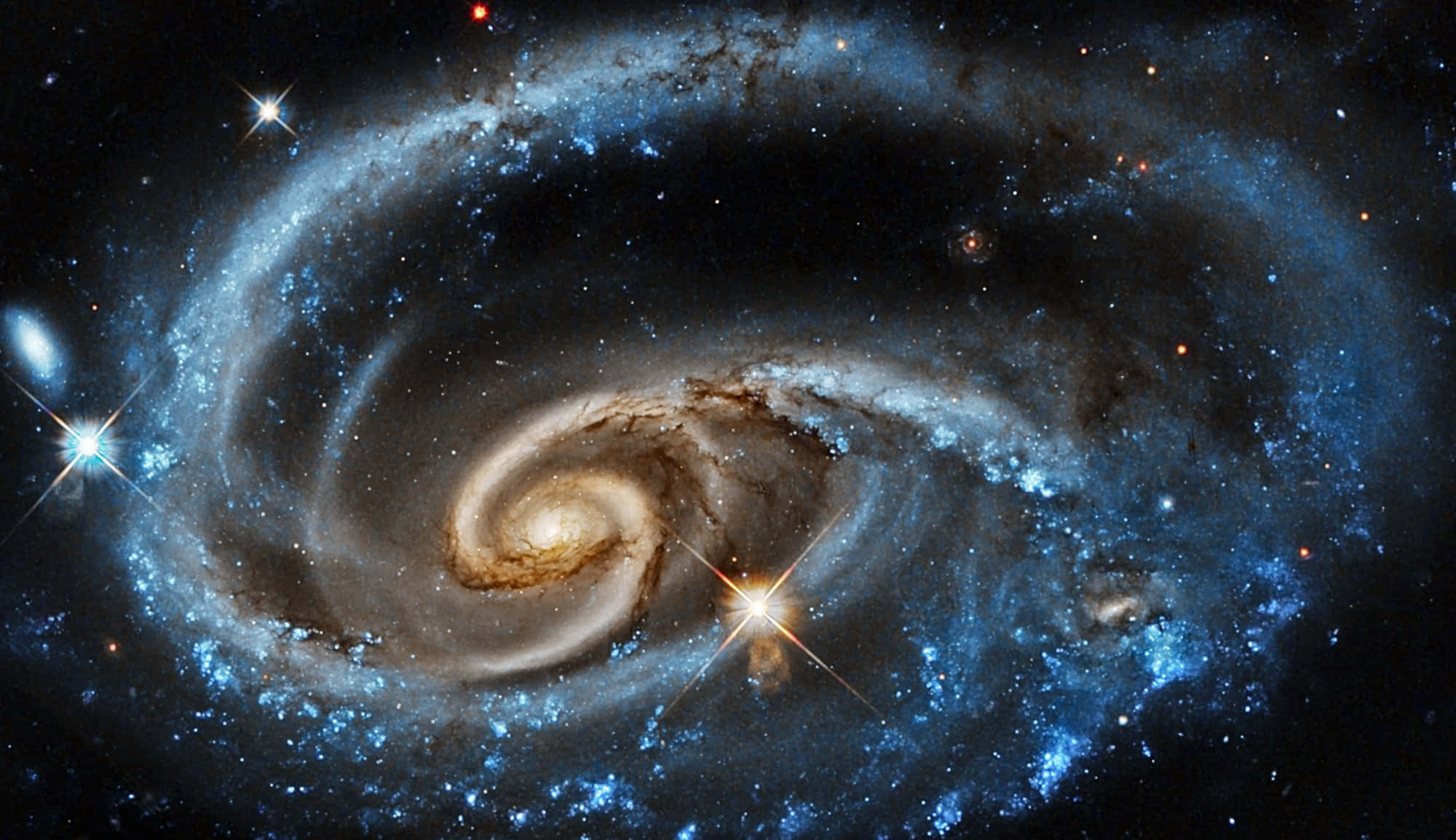美麗的NASA星系圖片 壁紙 — 一個令人嘆為觀止的螺旋星系，藍色星團和金色塵埃帶在繁星點點的宇宙虛空中旋轉。