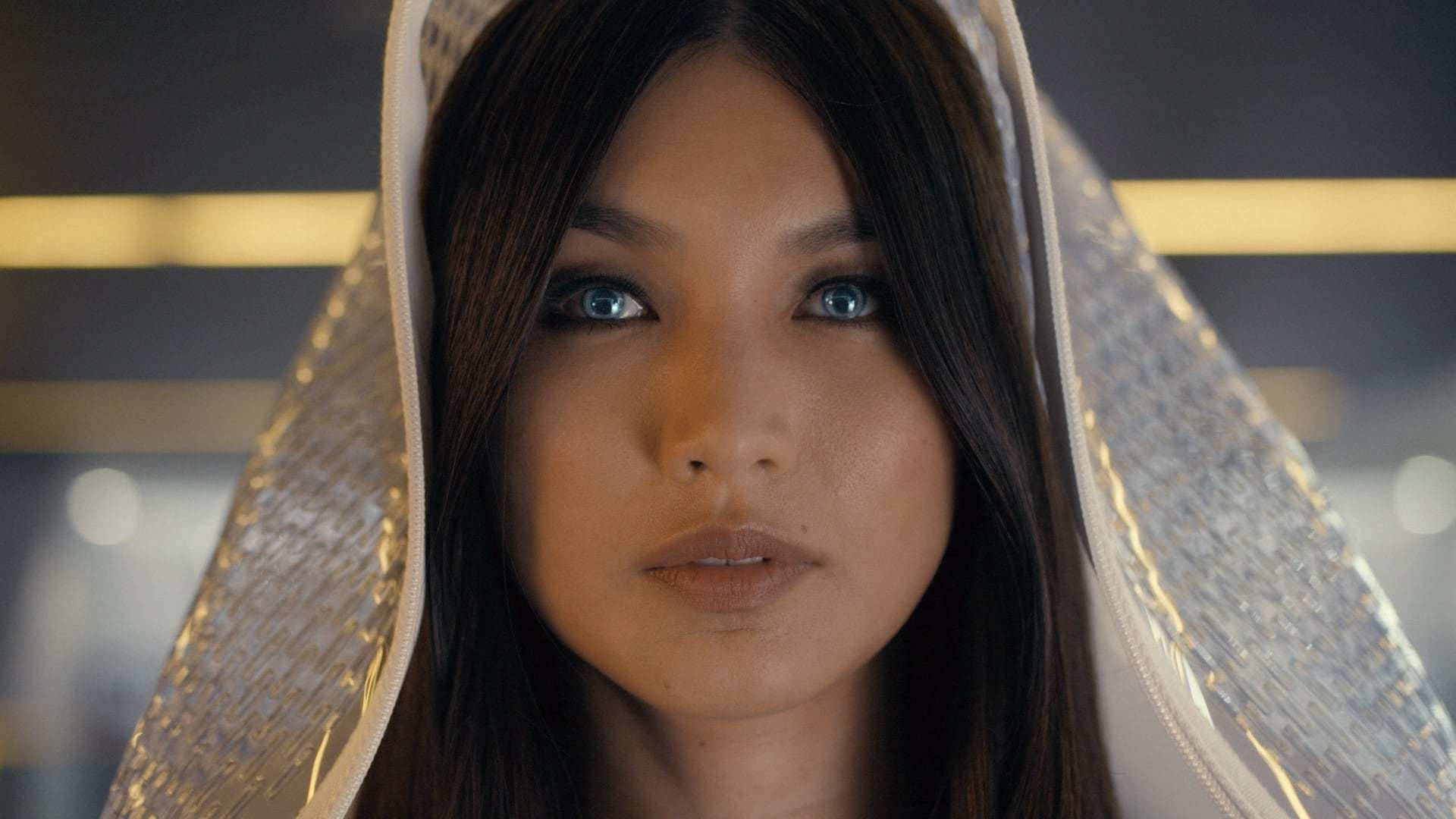 美麗的嘉瑪·陳 壁紙 — 一位女士的特寫肖像，擁有引人注目的藍色眼睛和深色頭髮，被閃閃發光的銀色連帽衣物所襯托。